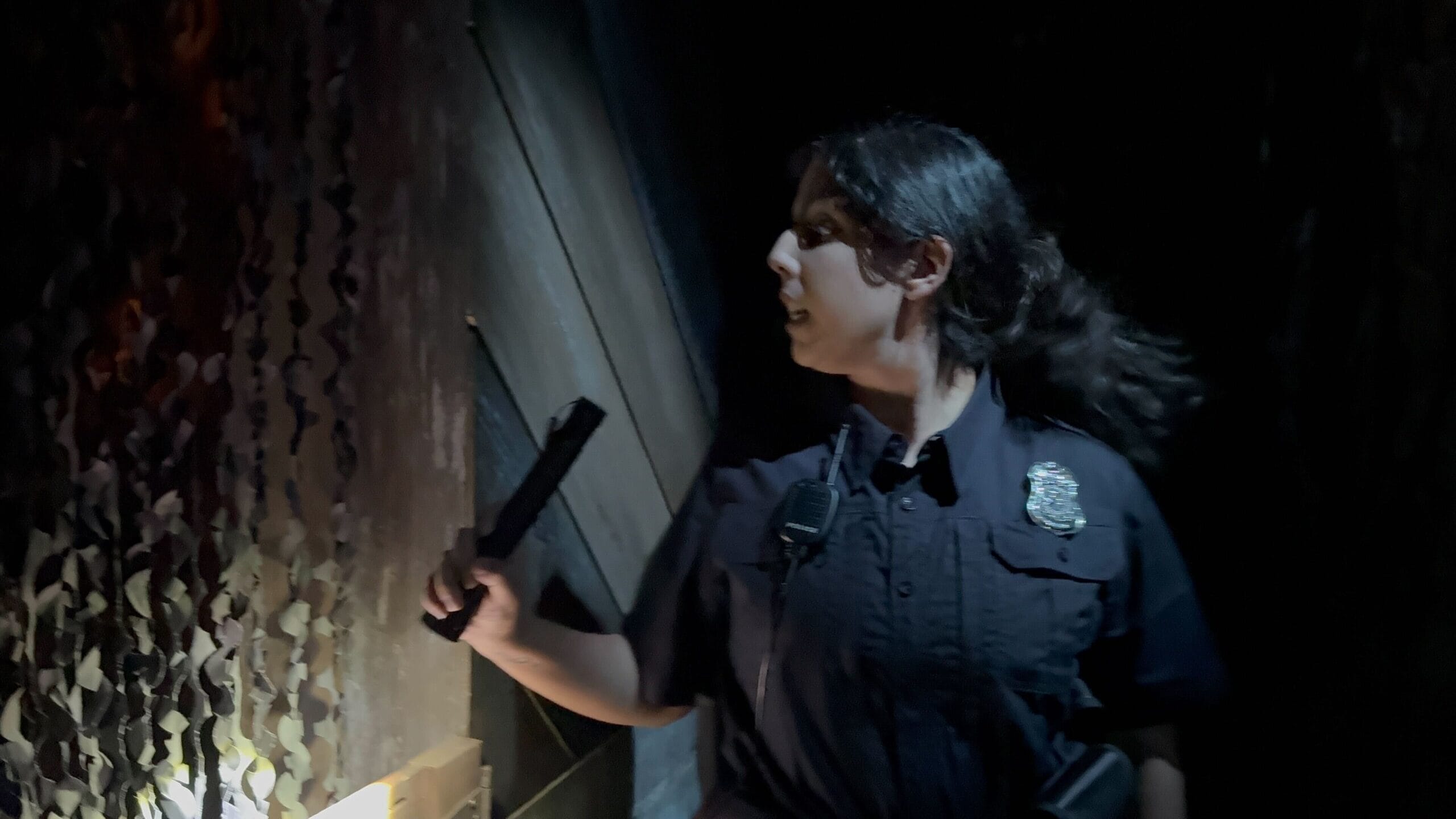 A police officer with a flashlight stands in the dimly lit Universal Horror Unleashed: The Exorcist: Believer House.