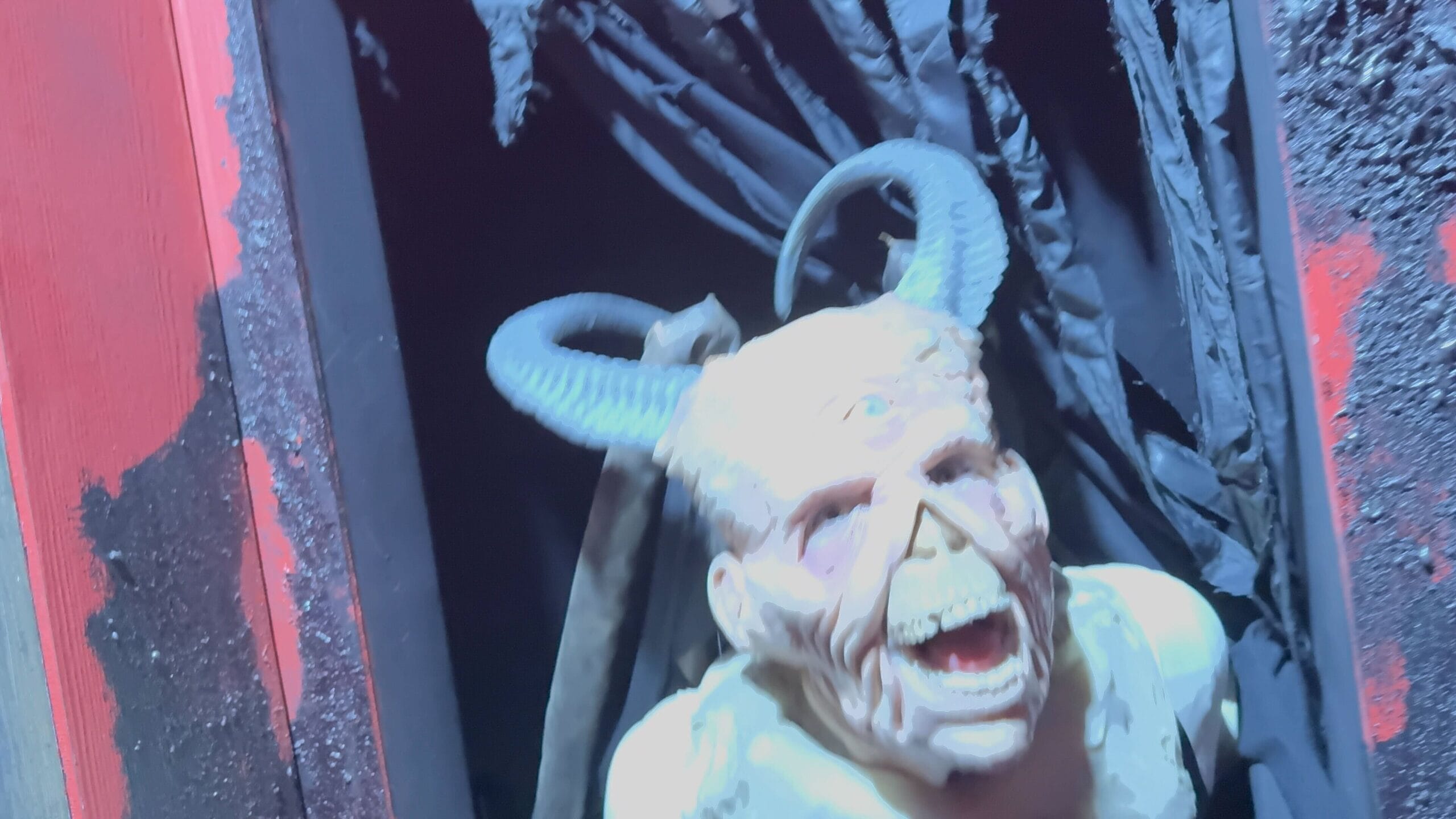 A scary demon with horns and sharp teeth emerges from a dark doorway at Believer House.