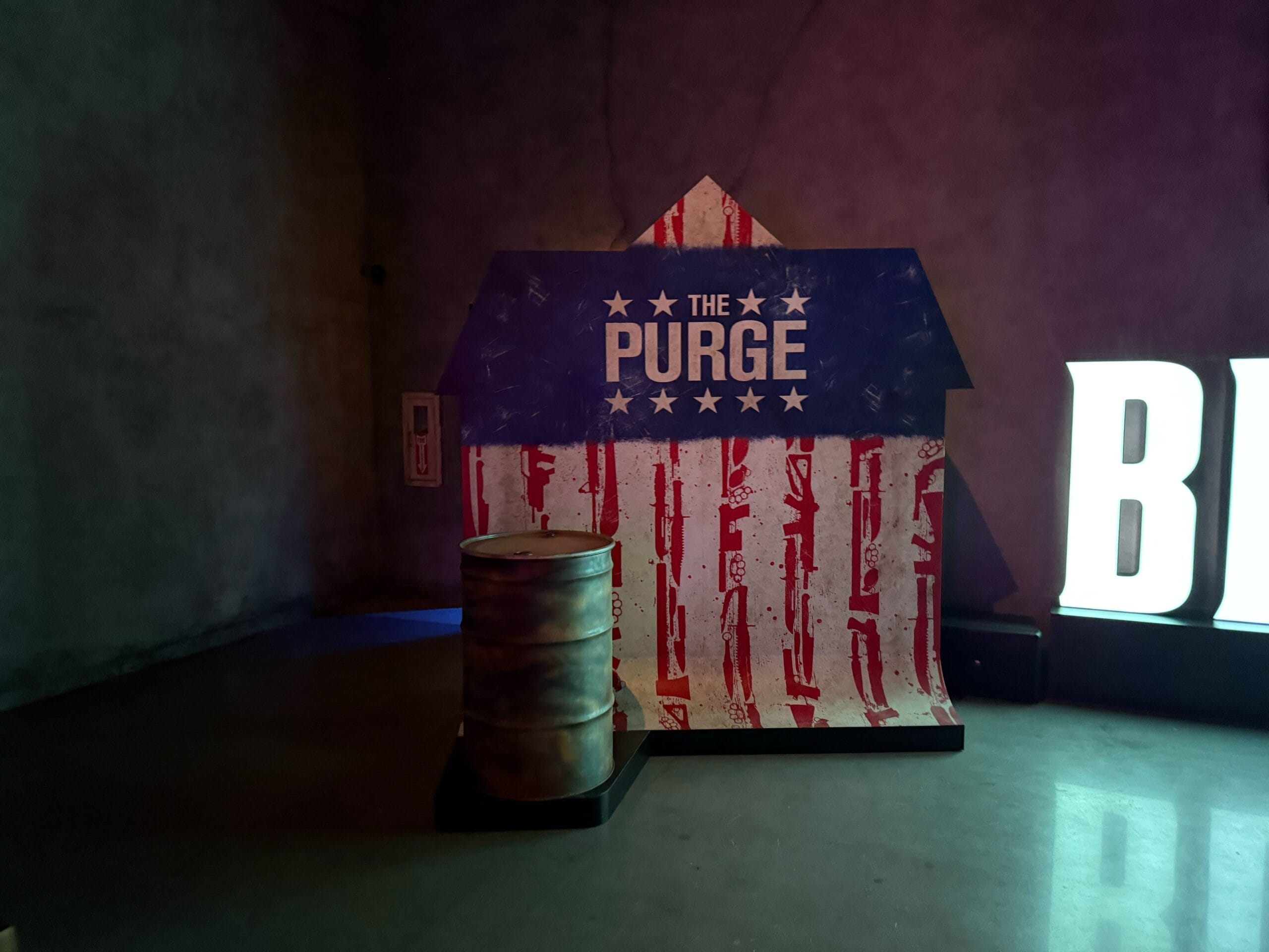 A "The Purge" sign with a red, white, and blue design stands behind a barrel at Universal Horror Unleashed Las Vegas.
