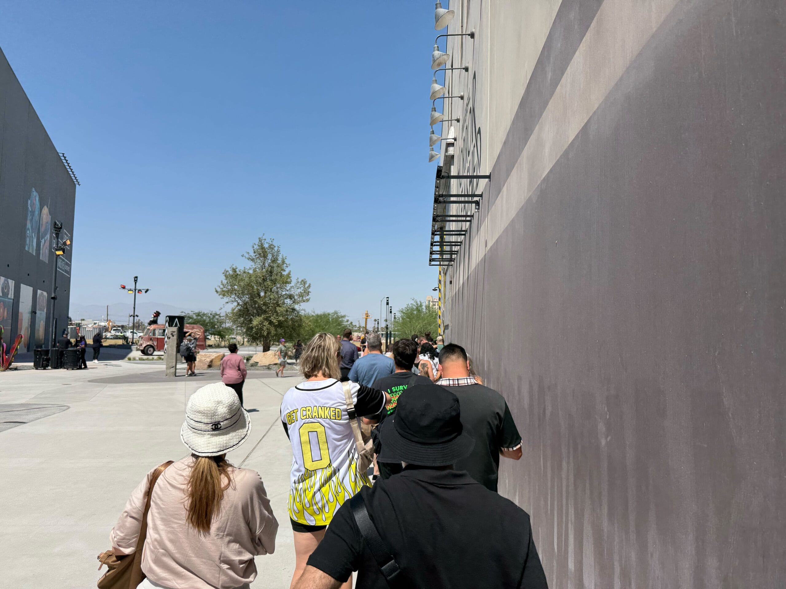 People stand in line outside a tall wall, waiting for a full tour under the clear Las Vegas sky on a sunny day.