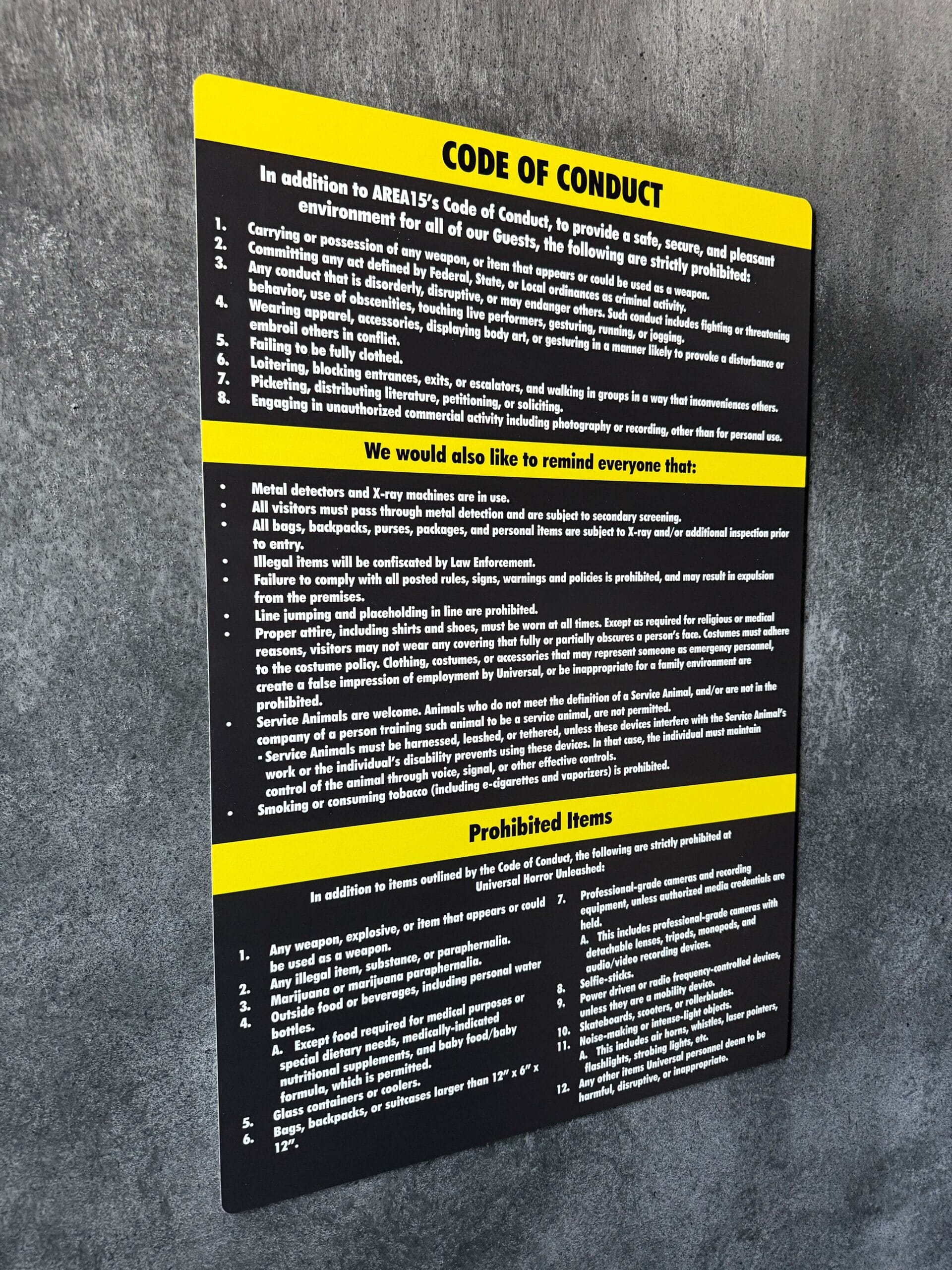 A black and yellow “Code of Conduct” sign for Full Tour at Las Vegas, mounted on a gray textured wall.