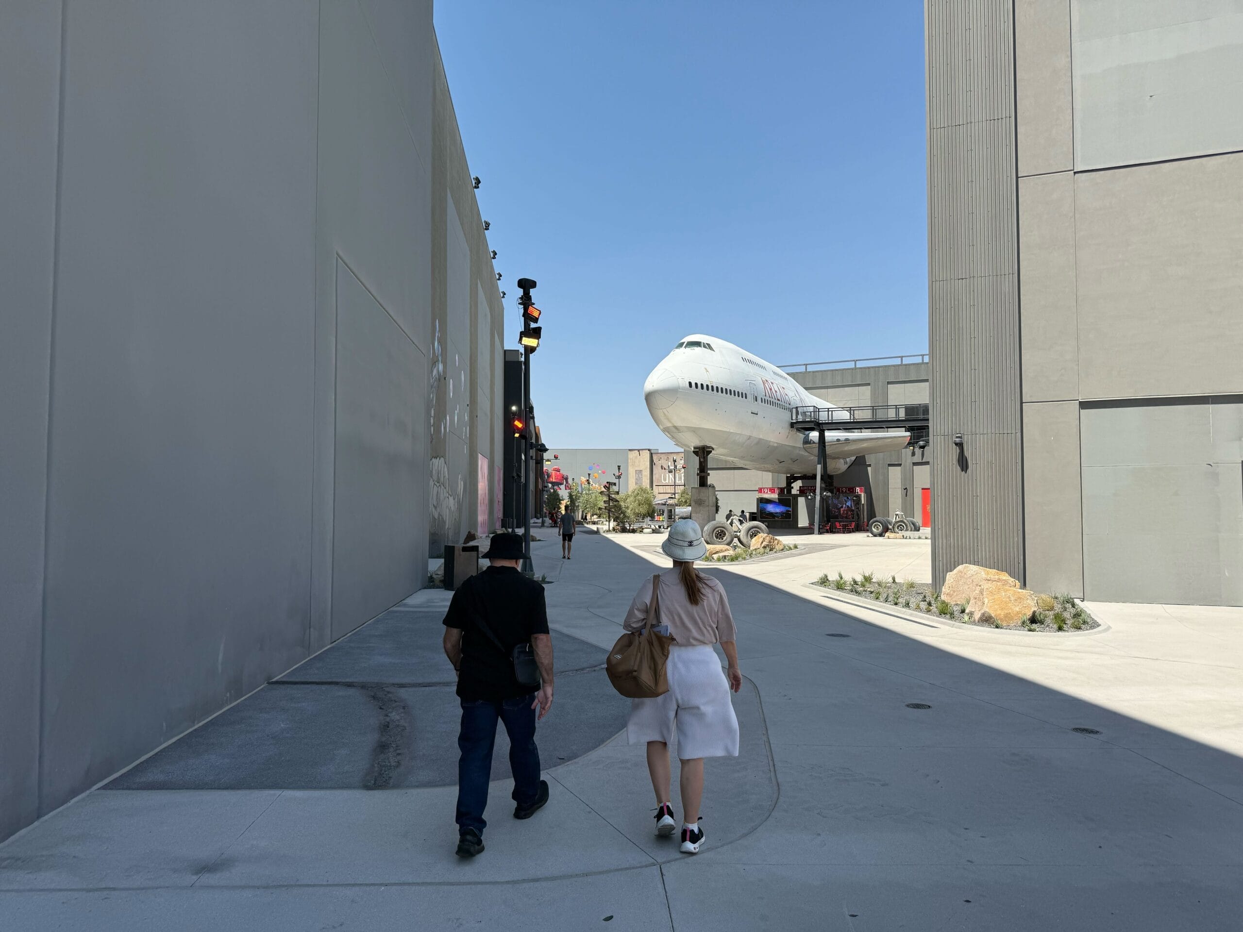 Two people walk toward a large airplane set piece in Las Vegas on a sunny day.