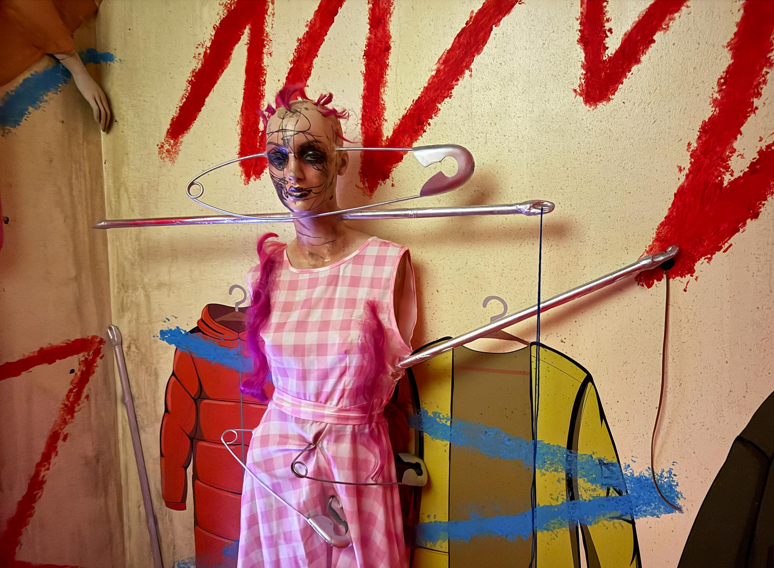 A mannequin in a pink dress and wig stands eerily, like a prop from HHN houses featuring flesh-eating demons.