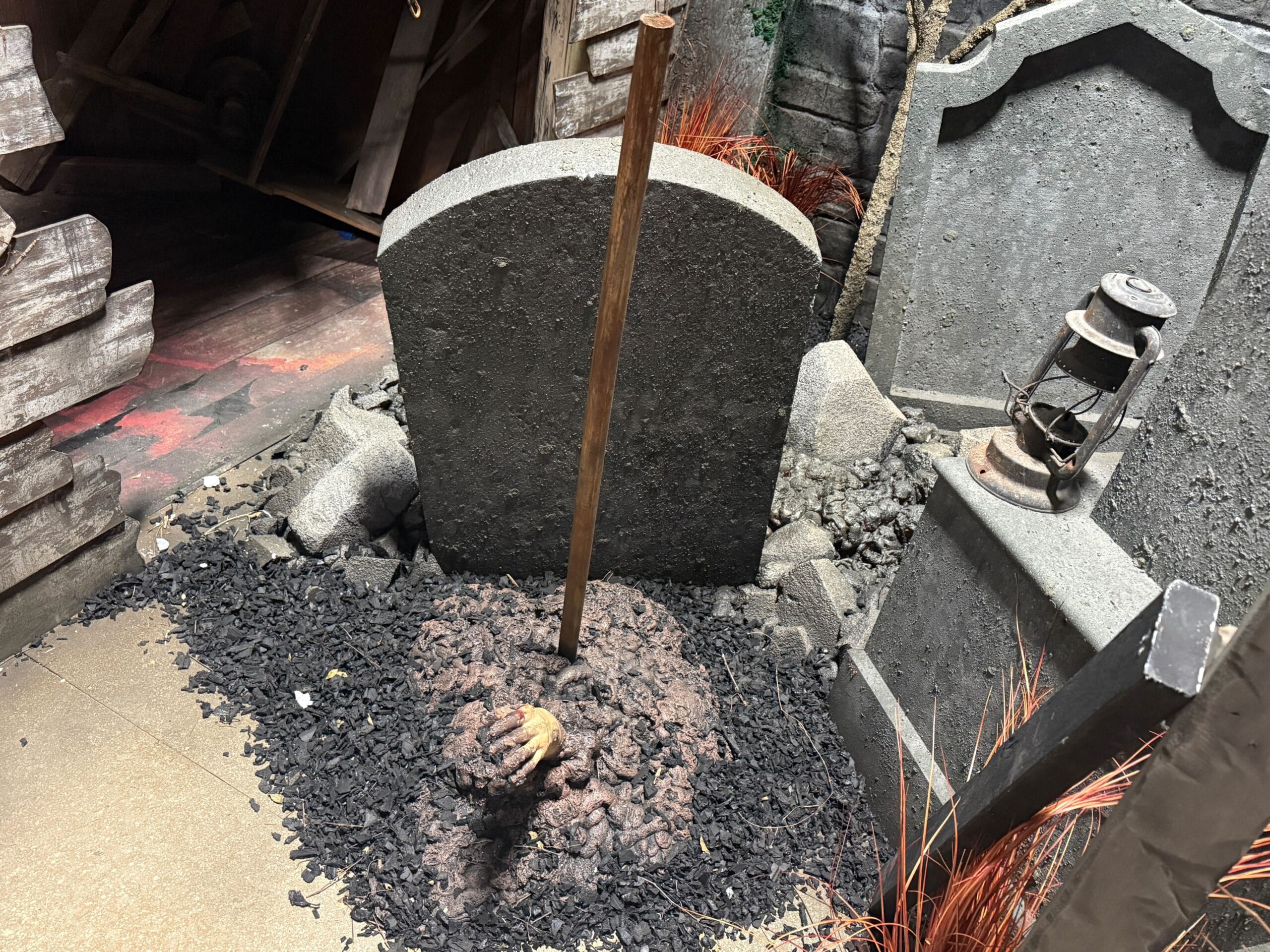 A fake hand emerges from soil in front of a gravestone, as if fleeing flesh-eating demons, in a spooky graveyard display.