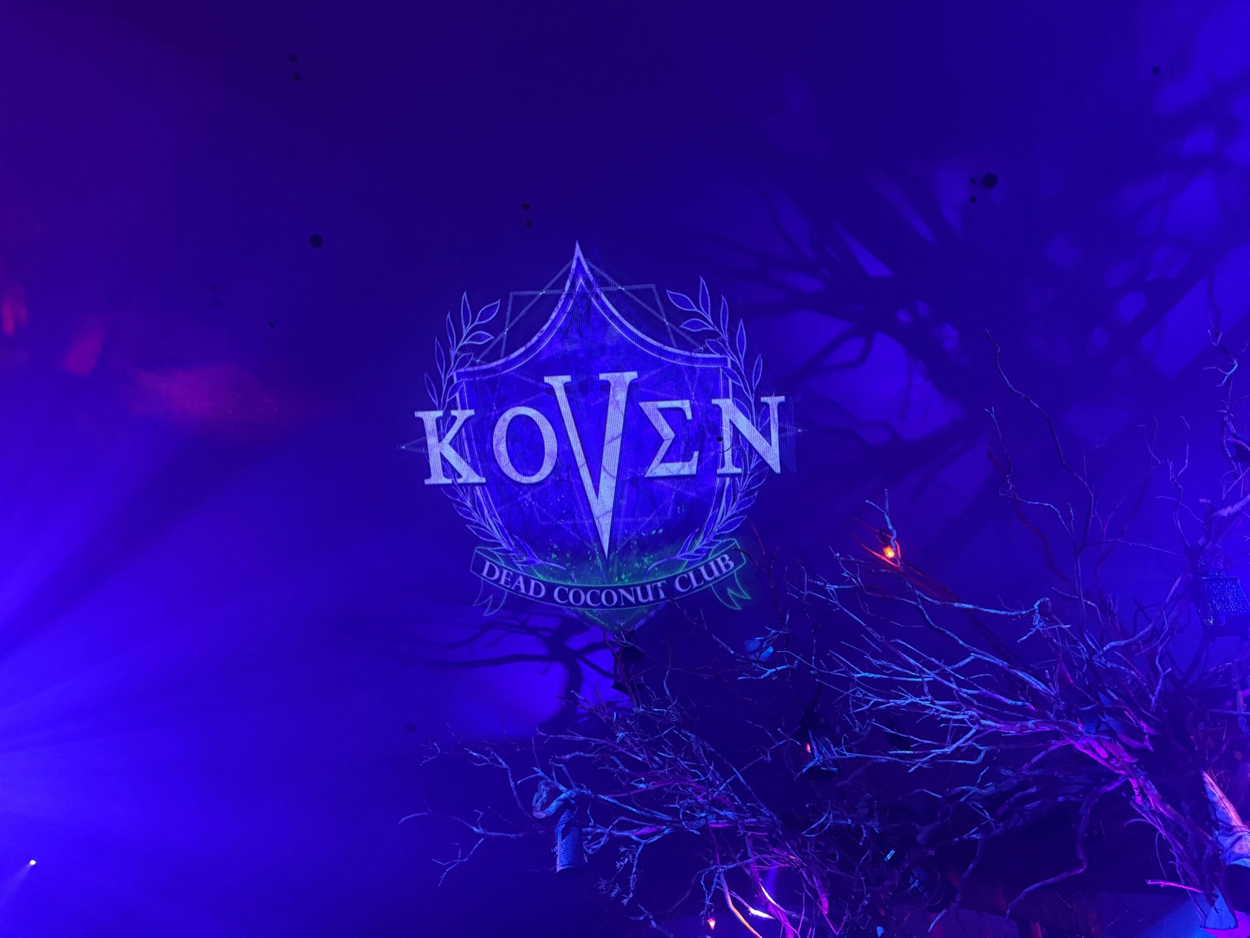 Blue and purple lights cast spooky shadows on the "Dead Coconut Club" logo, perfect for a Sorority Witches tour.