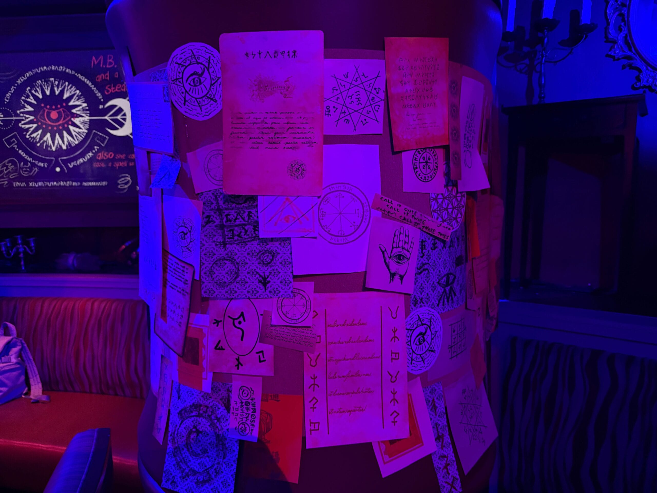 A pillar covered in hand-drawn occult symbols glows at the Sorority Witches’ Dead Coconut Club in a dimly lit room.