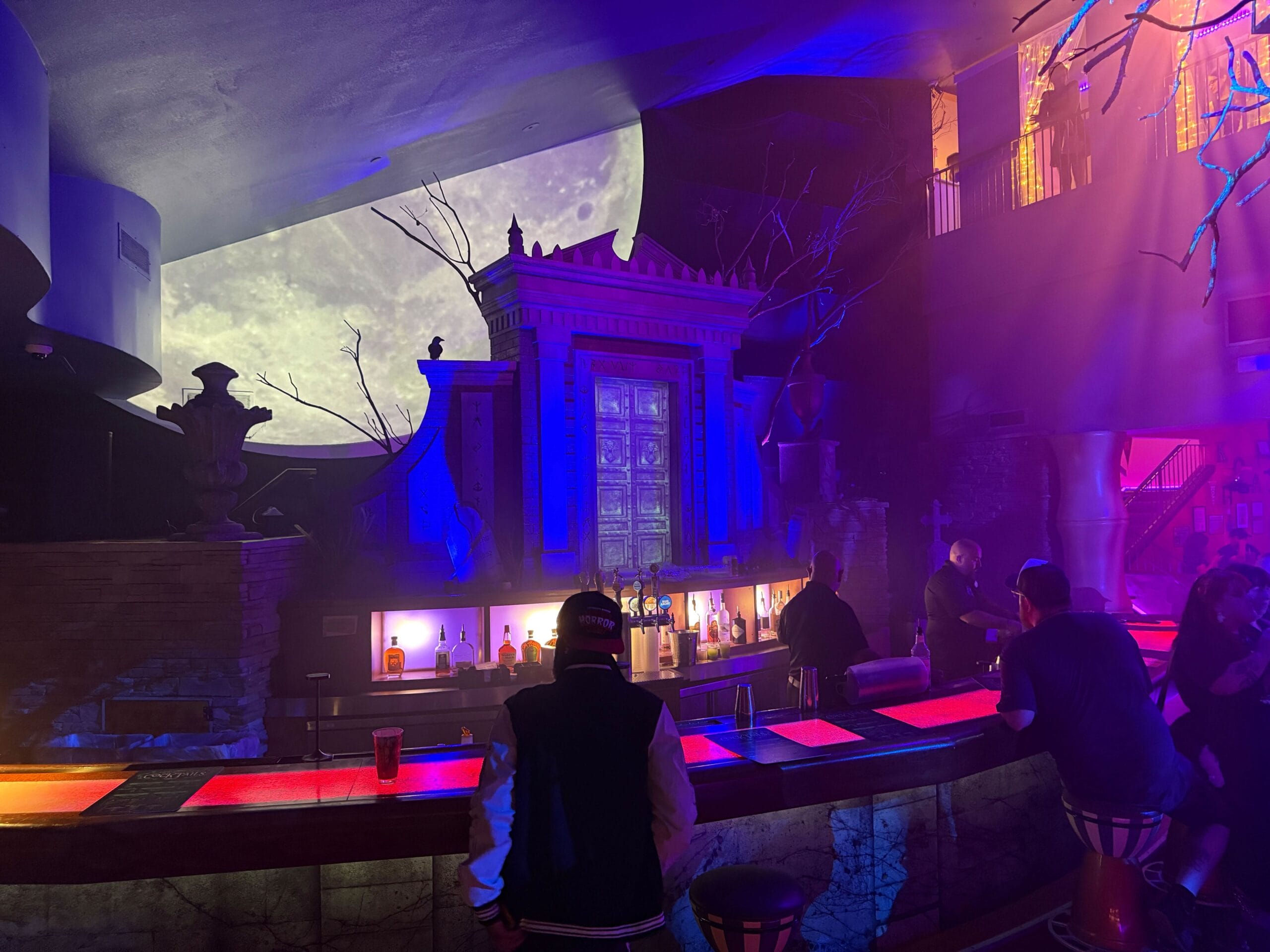 Bar with neon lighting, people seated, and a glowing moon backdrop—experience the magic at Dead Coconut Club.