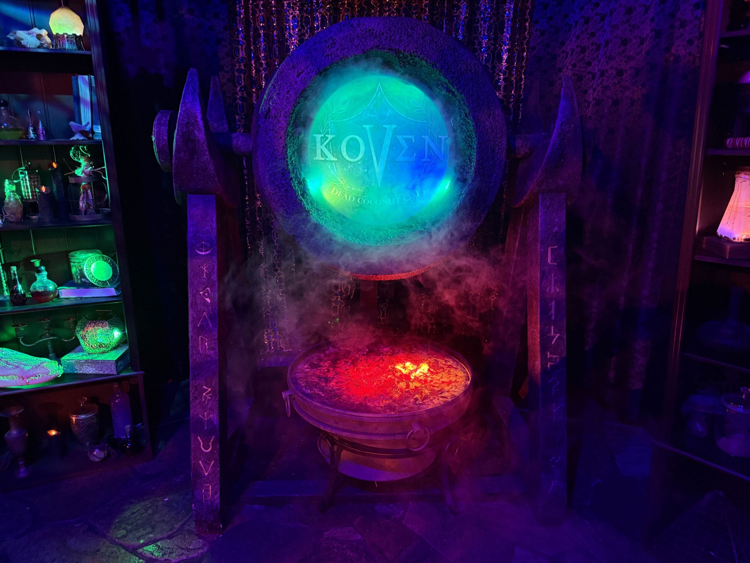 A glowing cauldron with mist sits under a "KOVEN" orb in the mystical Dead Coconut Club room.