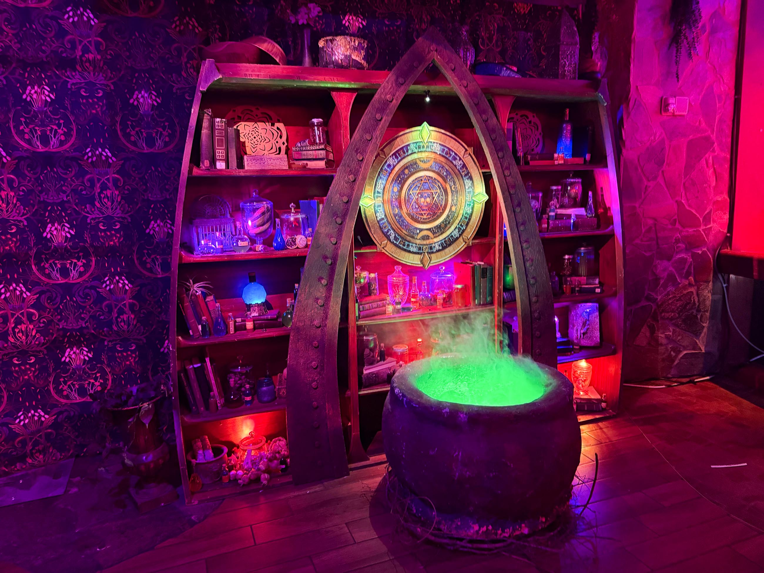 A glowing green cauldron sits before a mystical bookshelf, as Sorority Witches prepare for their Dead Coconut Club tour.