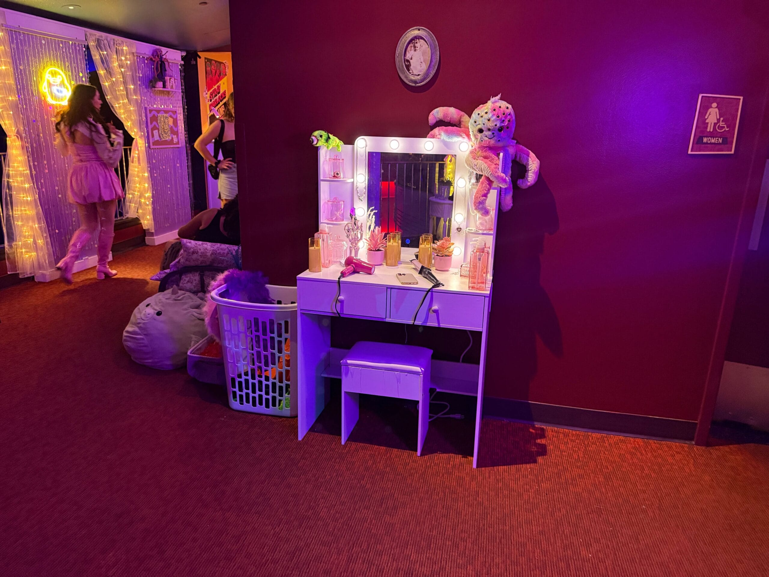 Vanity table with mirror and stuffed toys, glowing in purple at Dead Coconut Club; Sorority Witches tour vibes, lights behind.