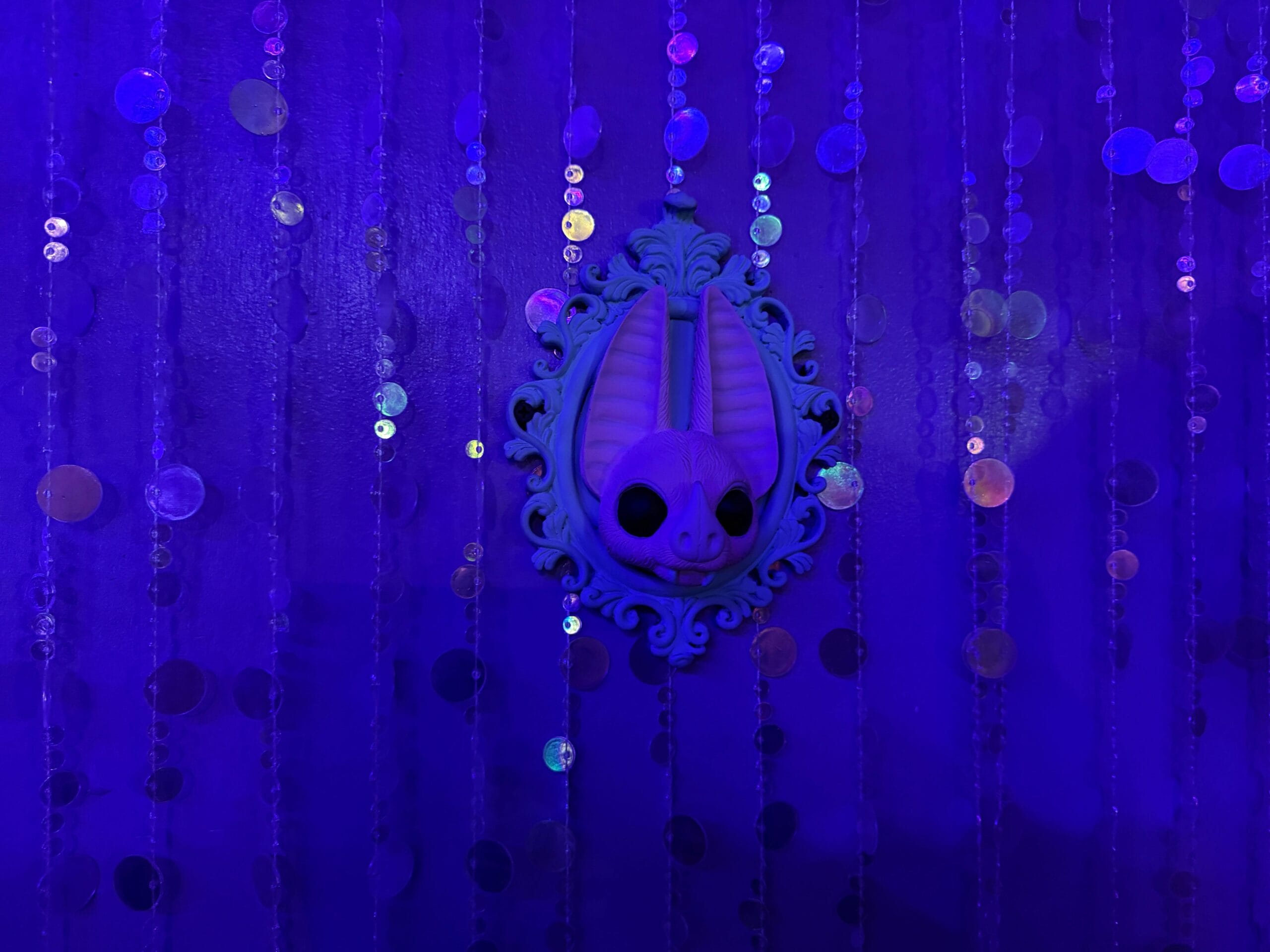 A framed rabbit skull from the Dead Coconut Club hangs on a purple wall with shimmering beaded strands.