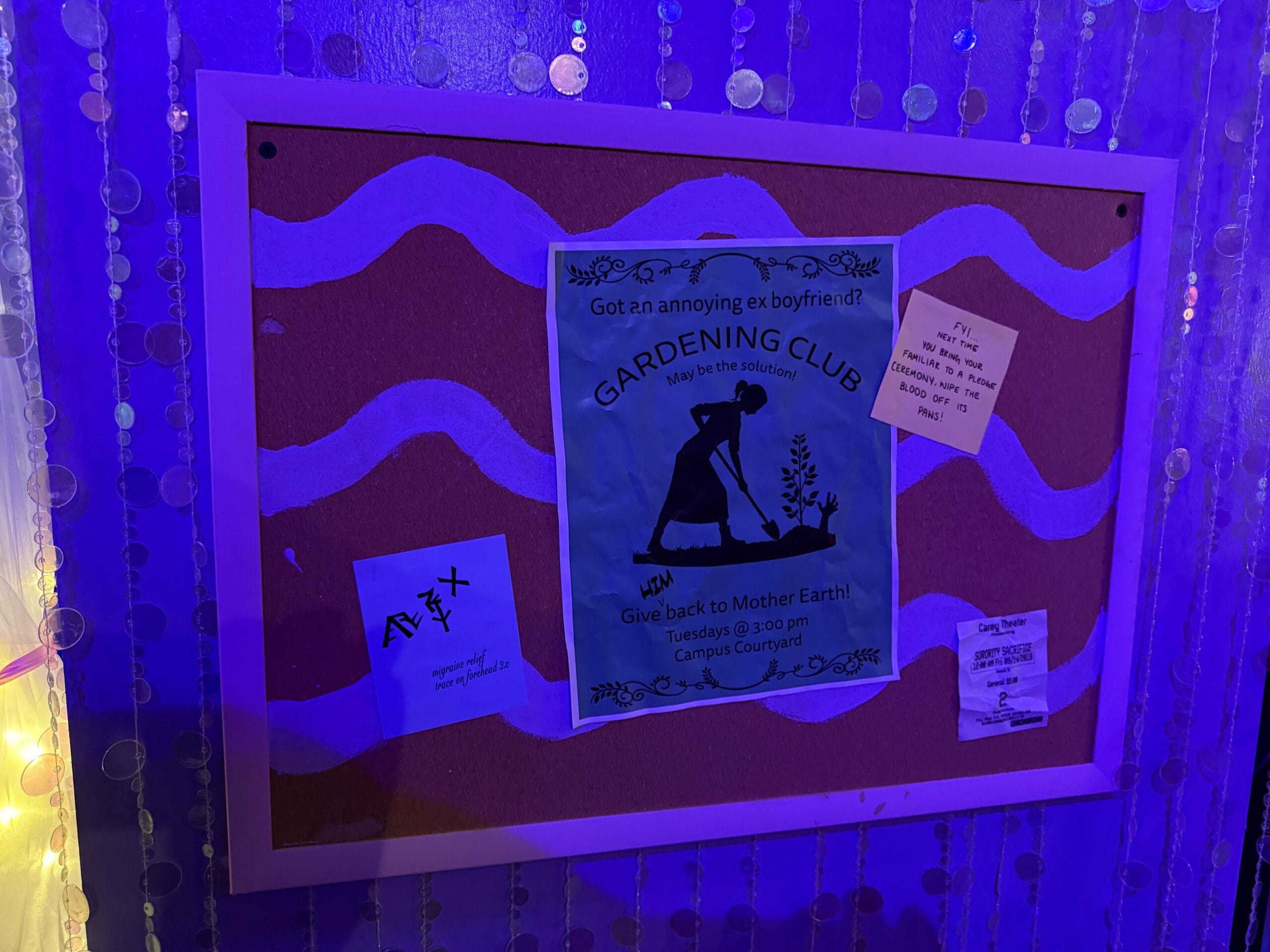 A corkboard with a Sorority Witches flyer and notes, bathed in purple light and adorned with hanging beads.
