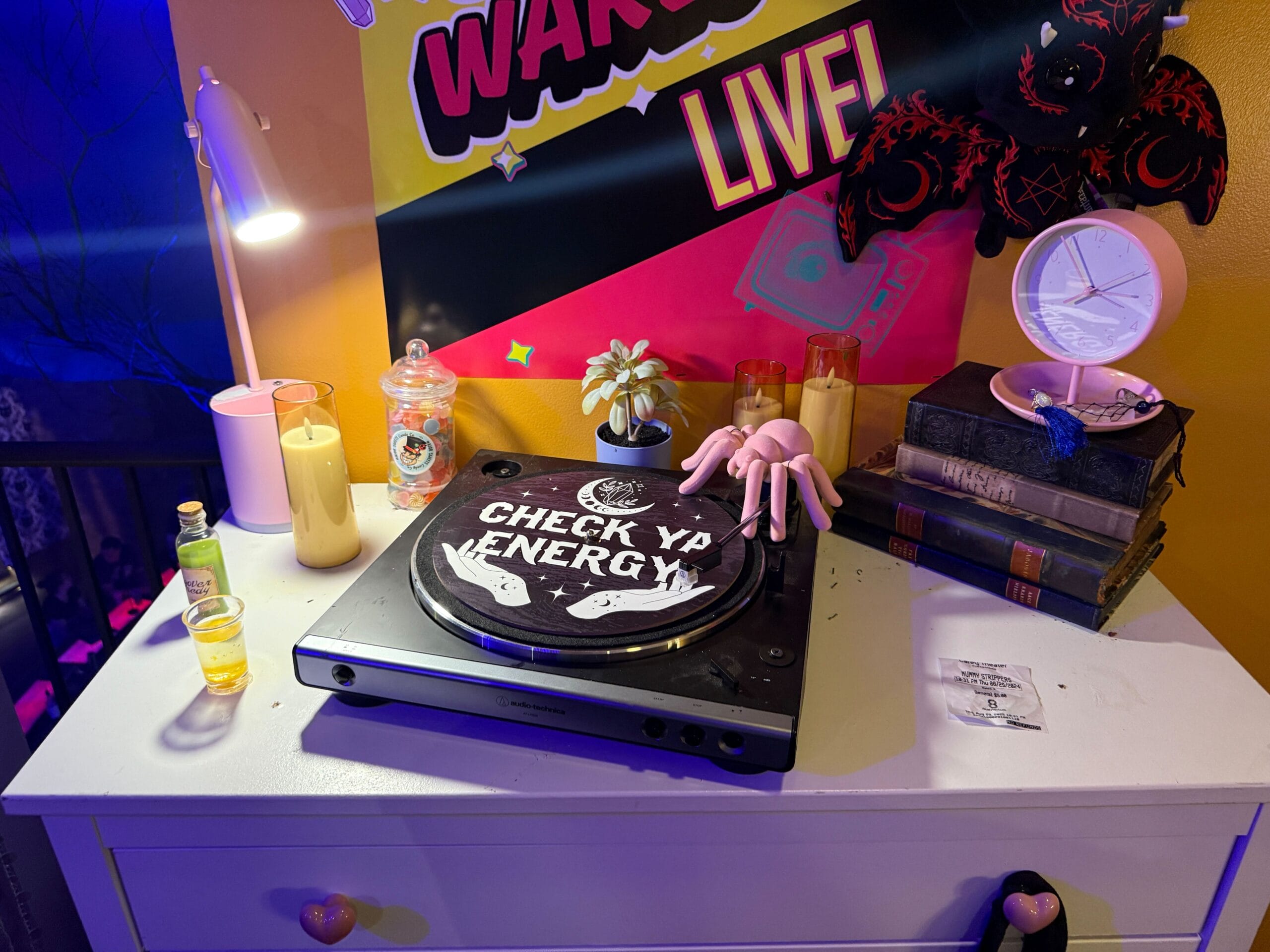A Sorority Witches turntable with "CHECK YA ENERGY" sits among candles, drinks, books, and decor.