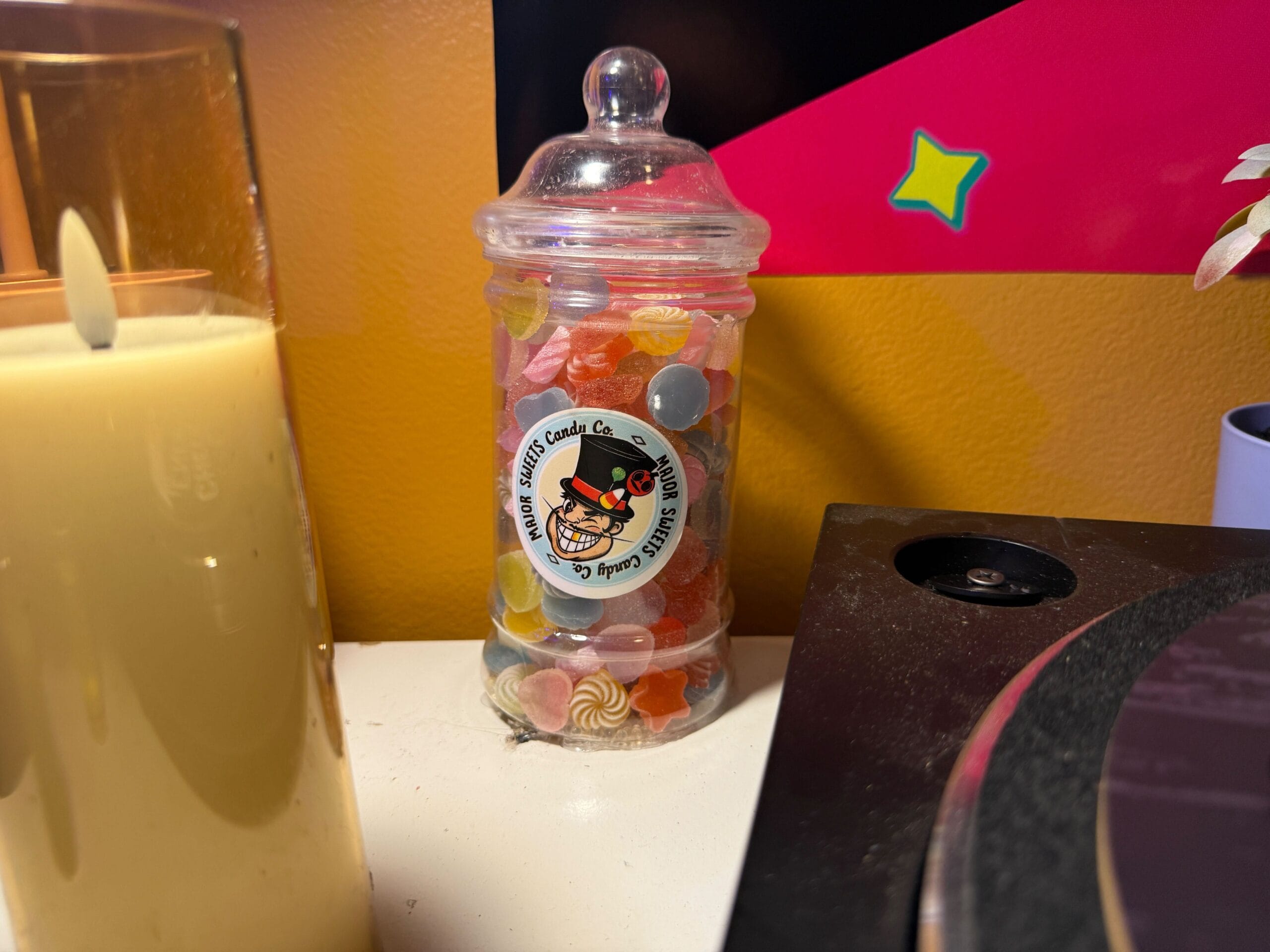 A glass jar of colorful candy sits beside a yellow candle at the Dead Coconut Club against a yellow and red wall.