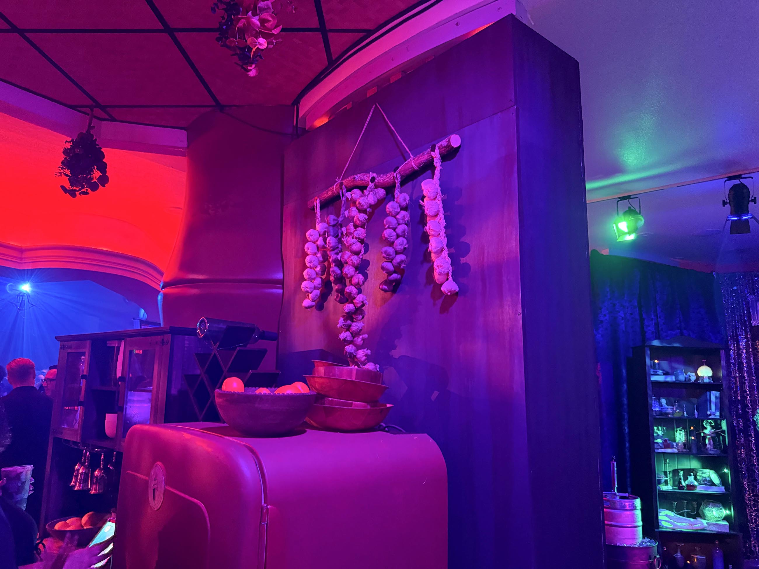 Dimly lit room at Dead Coconut Club with garlic and onions hanging, bowls below, and shelves of dishes behind.