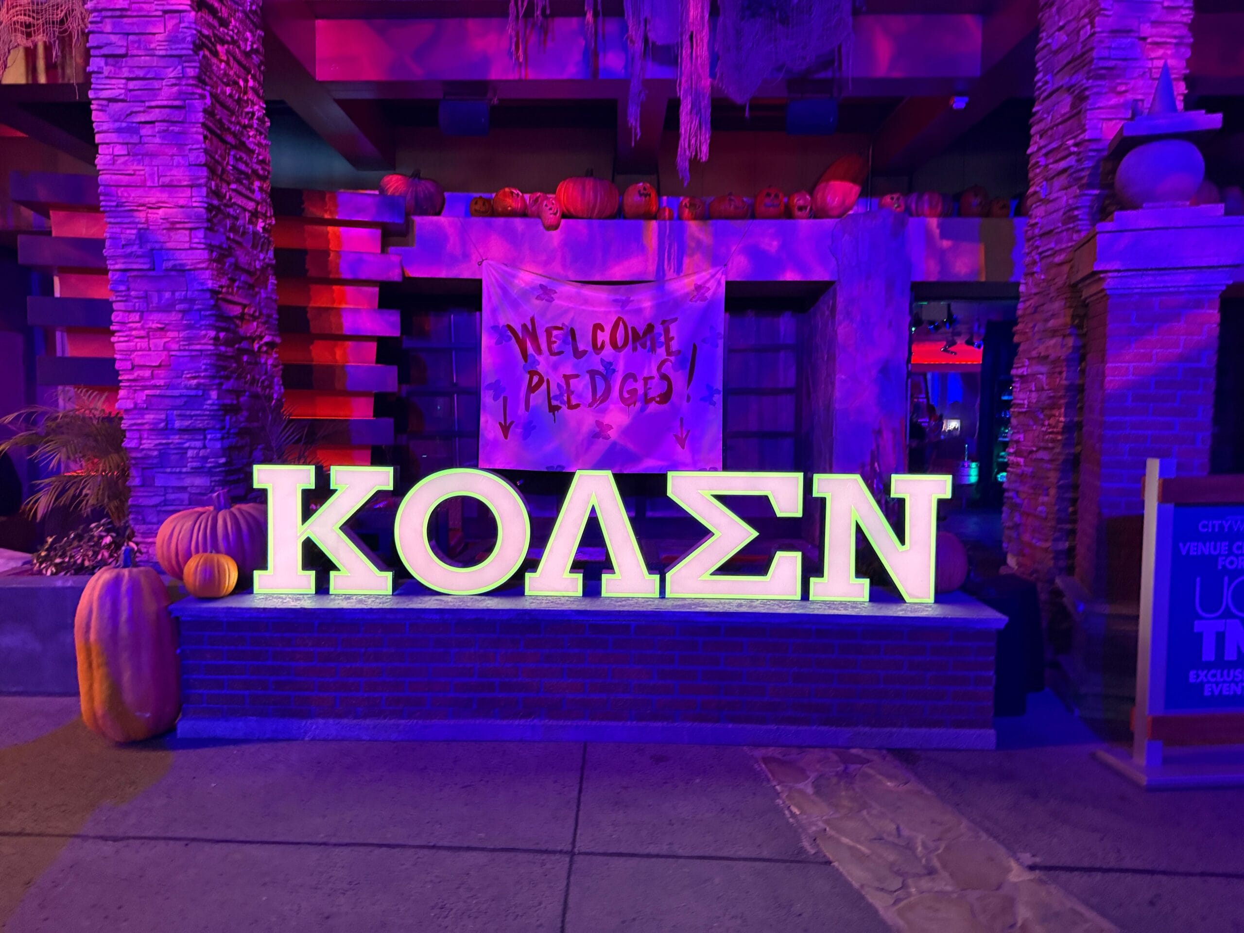 Large Greek letters and pumpkins glow before a “Welcome Pledges” sign at the Sorority Witches’ Dead Coconut Club.