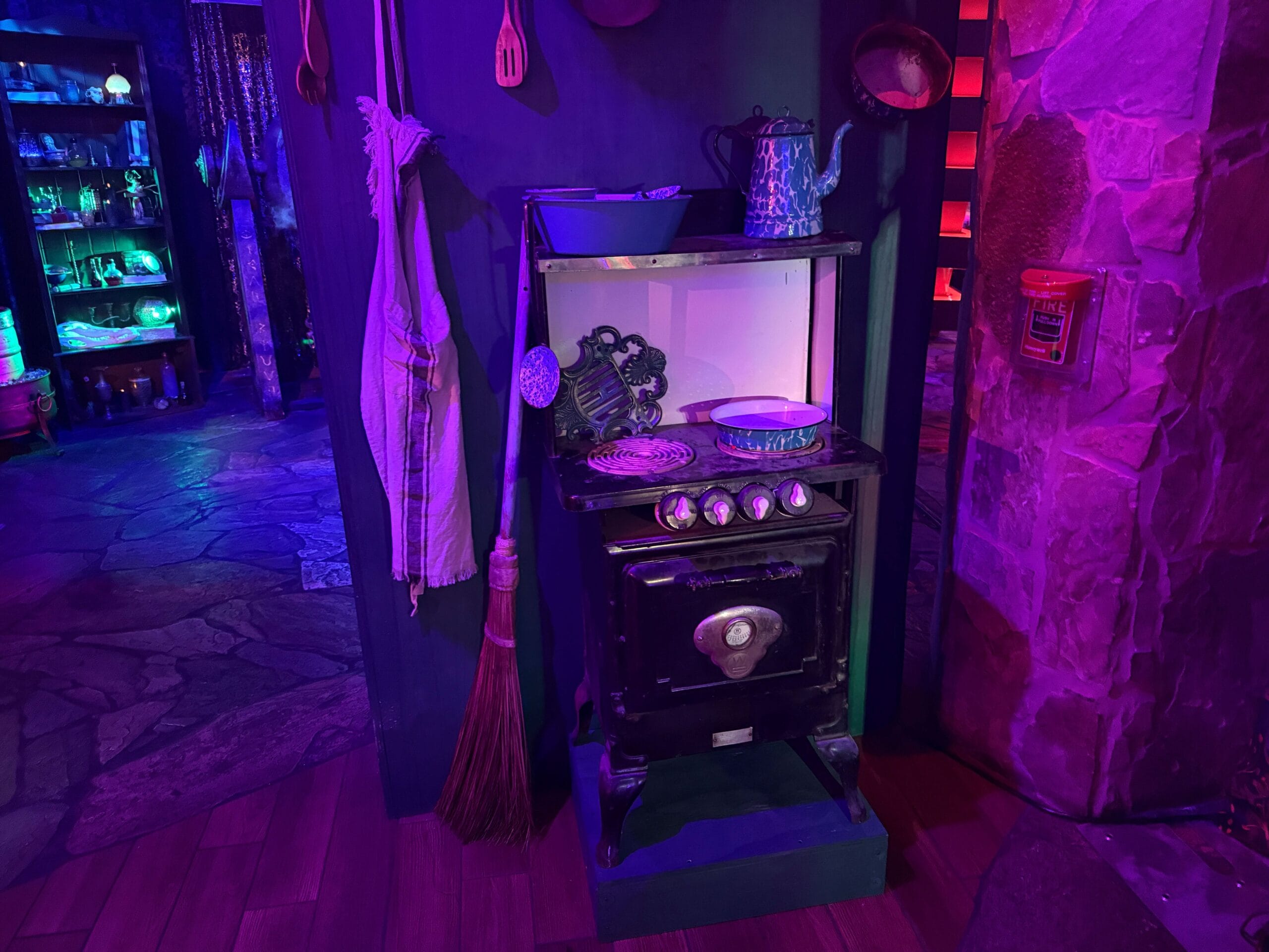 A vintage stove with pots, pans, and a broom in a whimsical room—perfect for Sorority Witches.