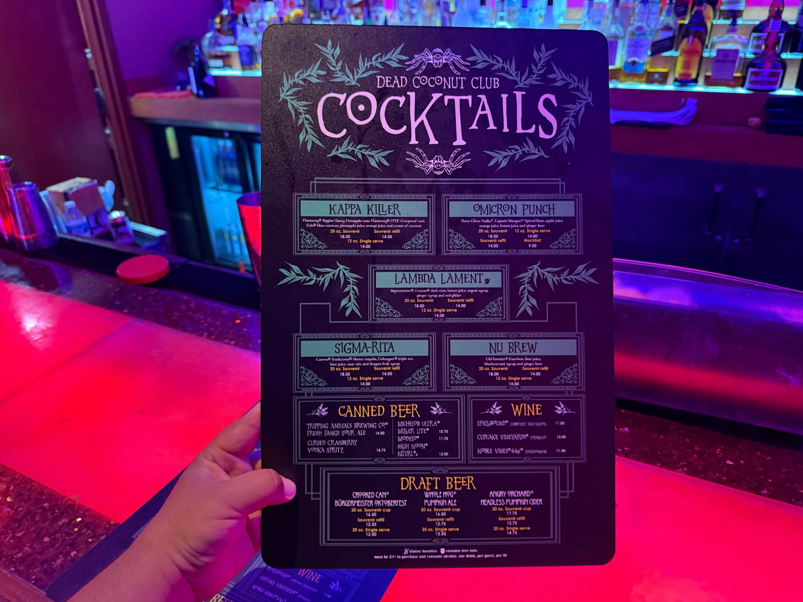 A hand holds a Dead Coconut Club cocktail menu in a dim bar, perfect for Sorority Witches on their Full Tour.