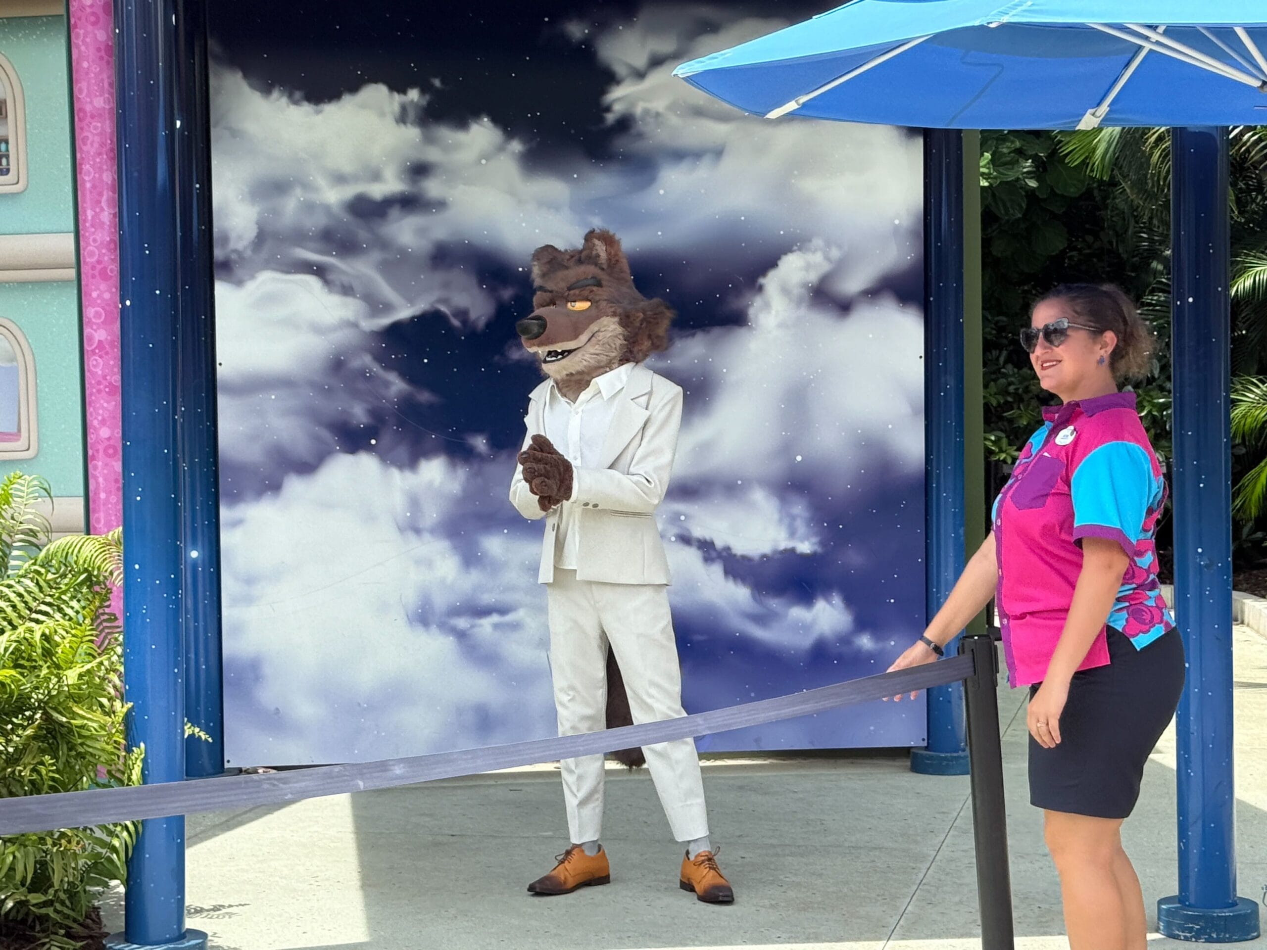 A person in a Mr. Wolf costume and white suit poses near staff at Universal Studios Florida under a blue umbrella.