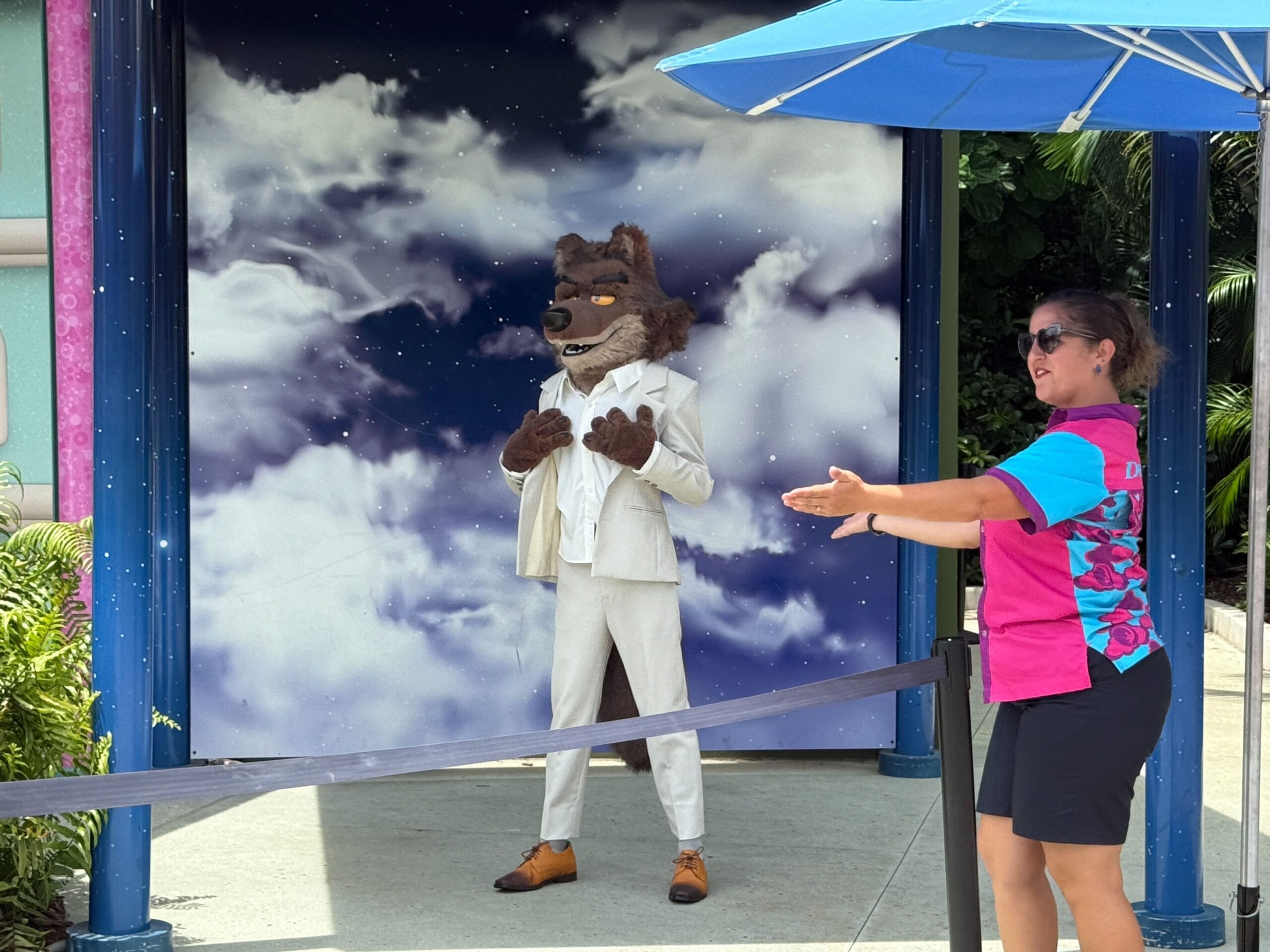 A person as Mr. Wolf from Bad Guys Films poses with a staff member at Universal Studios Florida’s cloudy sky backdrop.