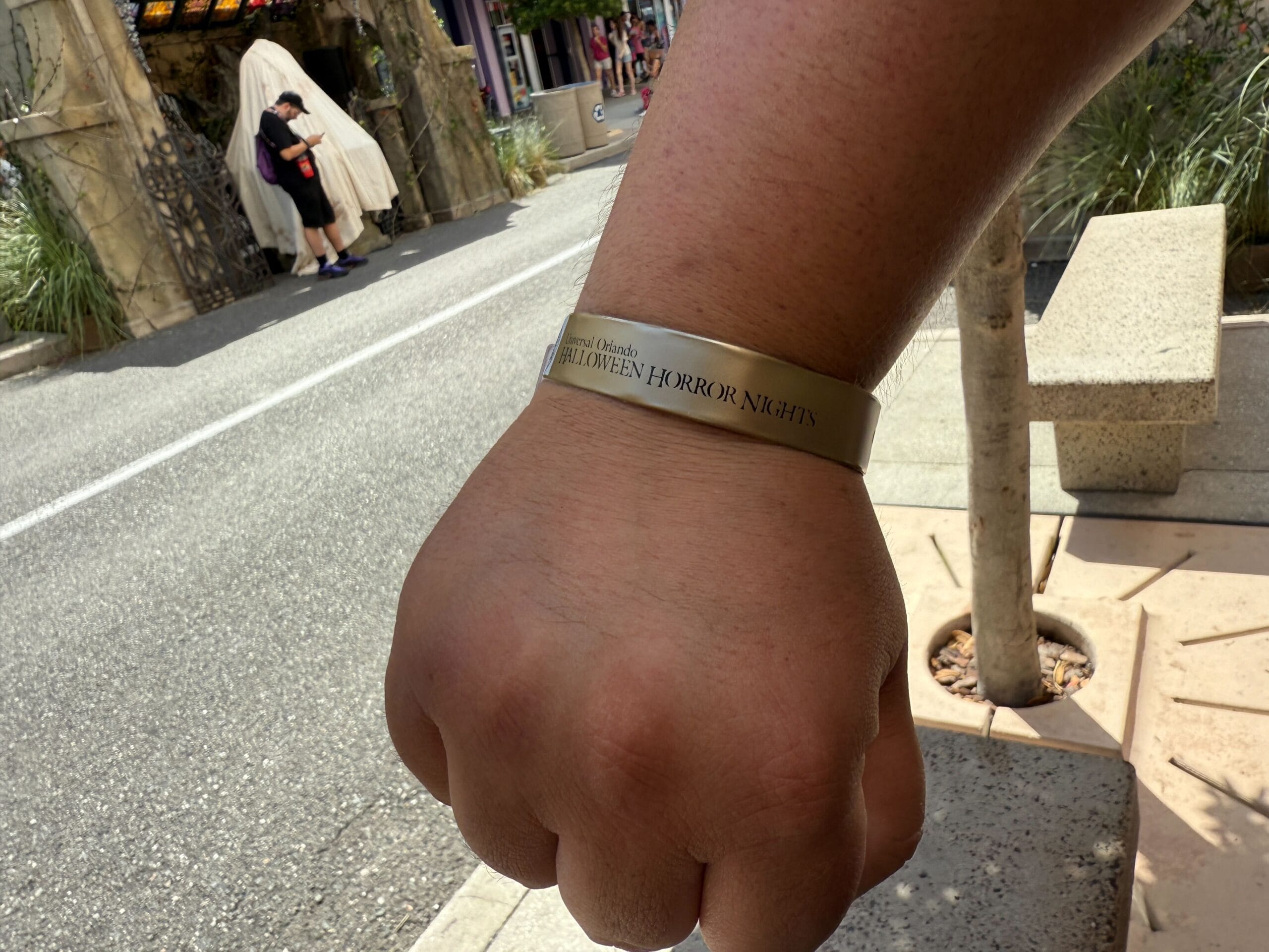 A close-up of a Stay and Scream wristband for Halloween Horror Nights 2025 on a person’s wrist, outdoors by a street.
