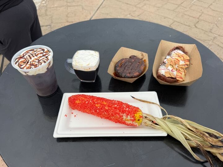 A table in the Jason Universe holds two hot drinks, dessert pastries, and seasoned corn with husk on a white tray.