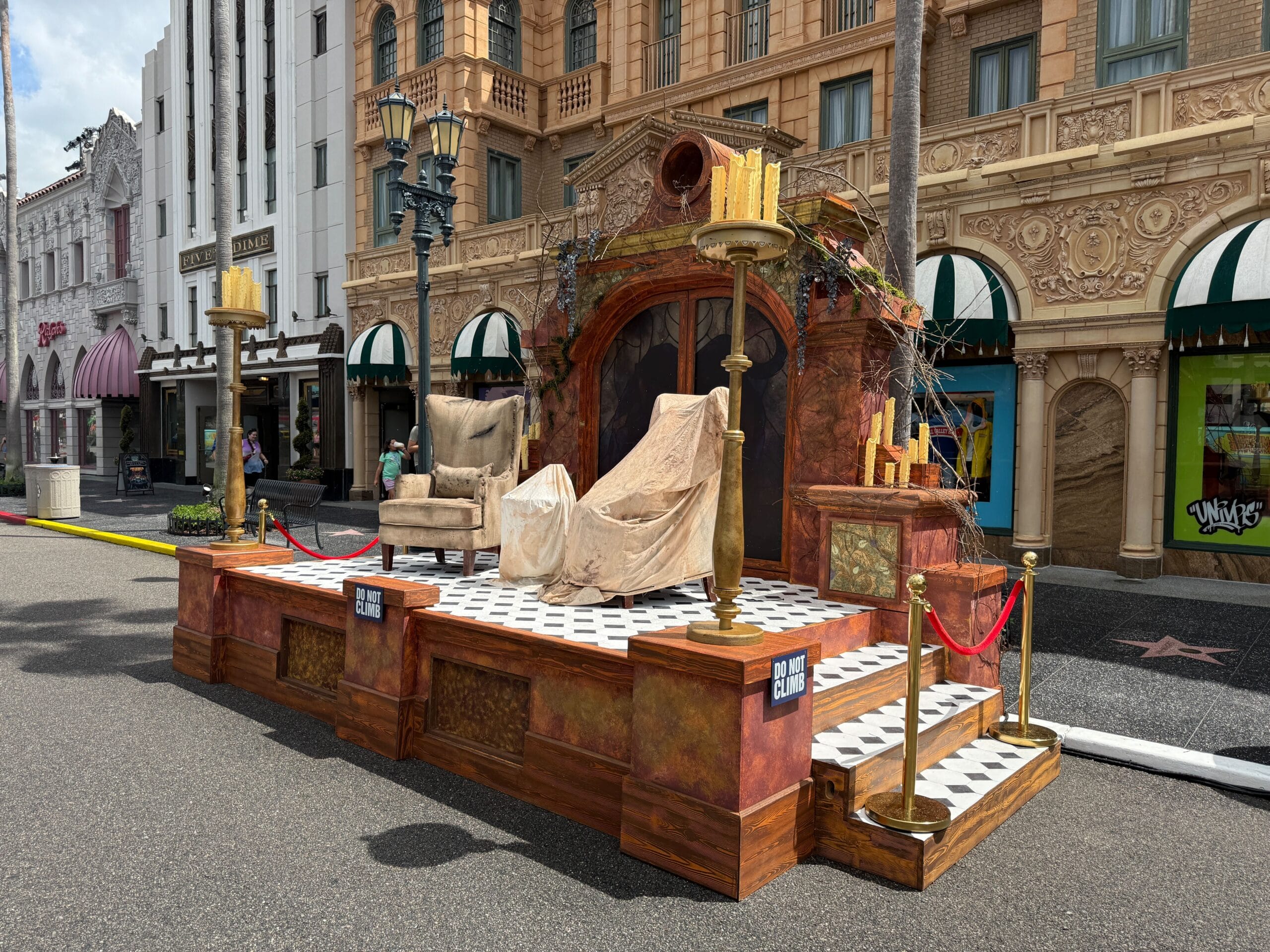 Outdoor stage with gothic decor, two chairs, and candles—perfect for Halloween Horror Nights 34 in front of city shops.