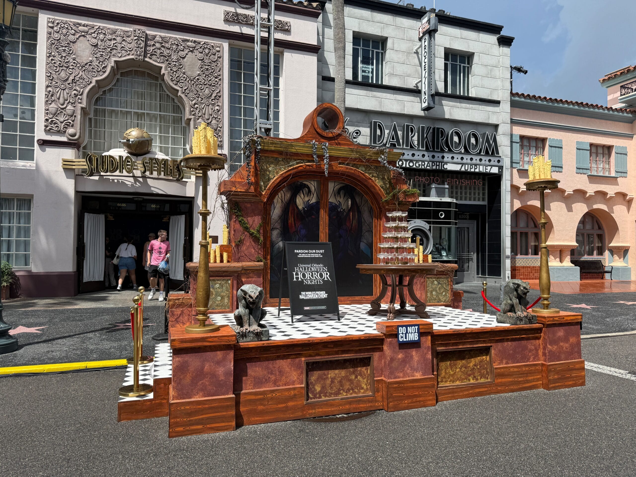 A spooky photo op with gothic decor and gargoyle statues stands outside Halloween Horror Nights 34 themed storefronts.