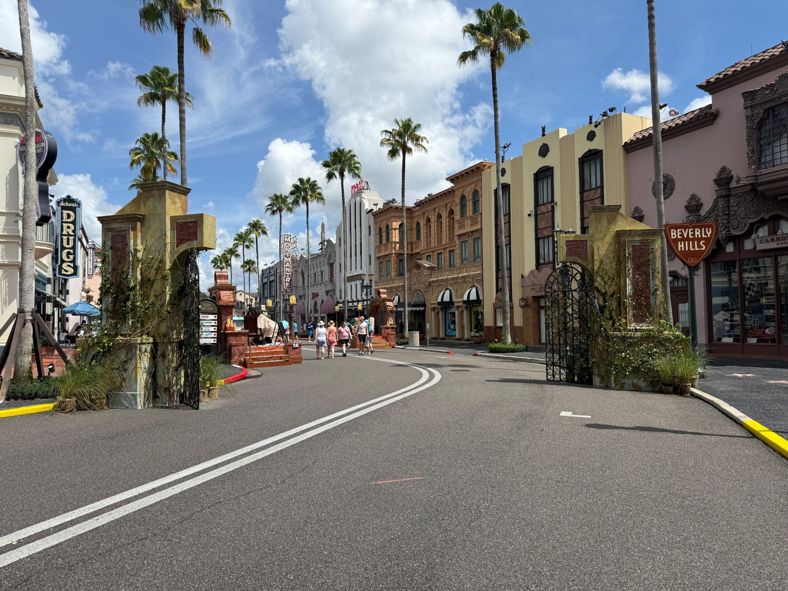 A sunny street lined with palm trees, shops, and Halloween Horror Nights 34 decorations welcomes people at the entrance.