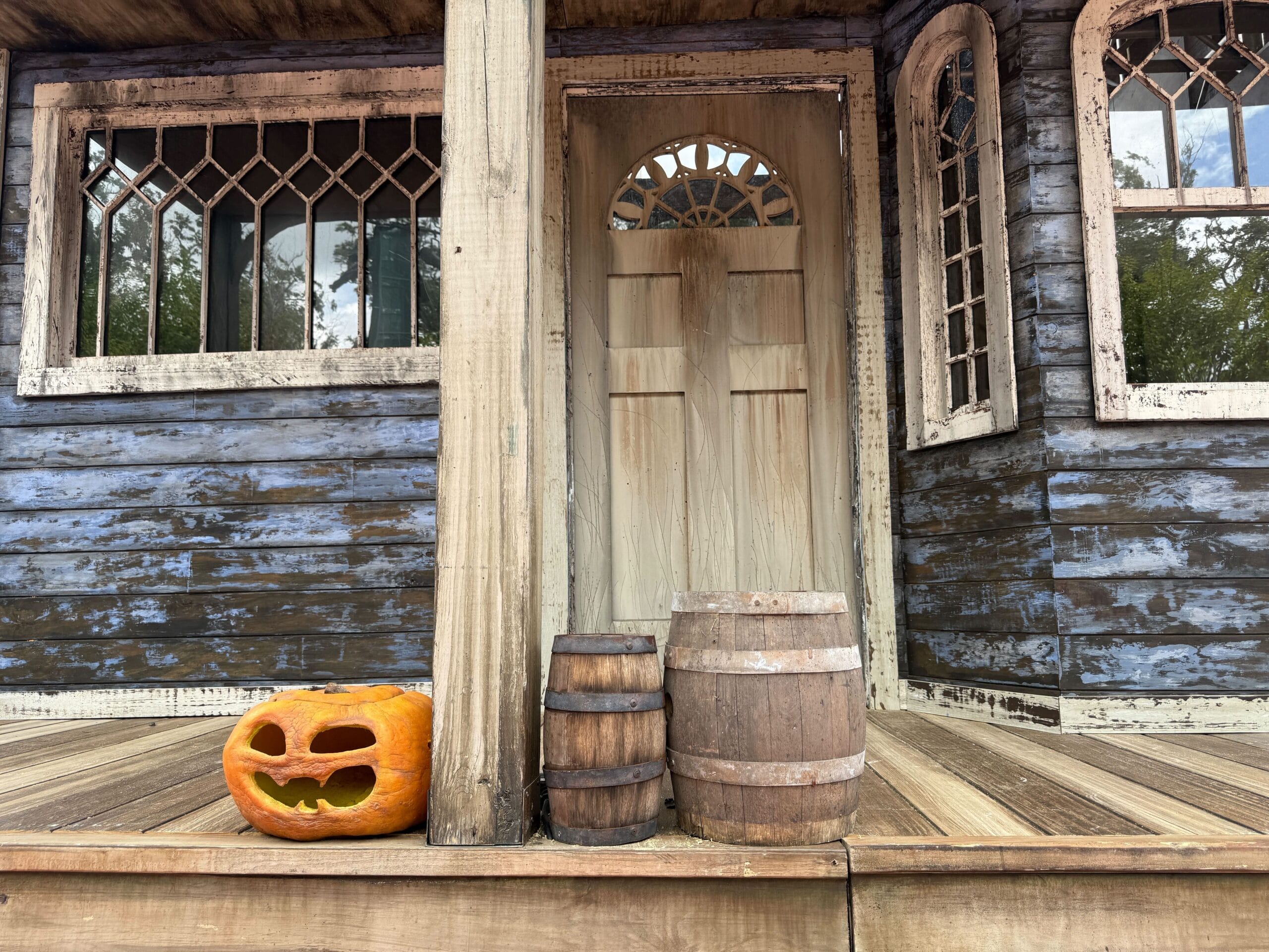 A carved pumpkin and two barrels sit on the porch, beneath a Halloween Horror Nights 34 sign.