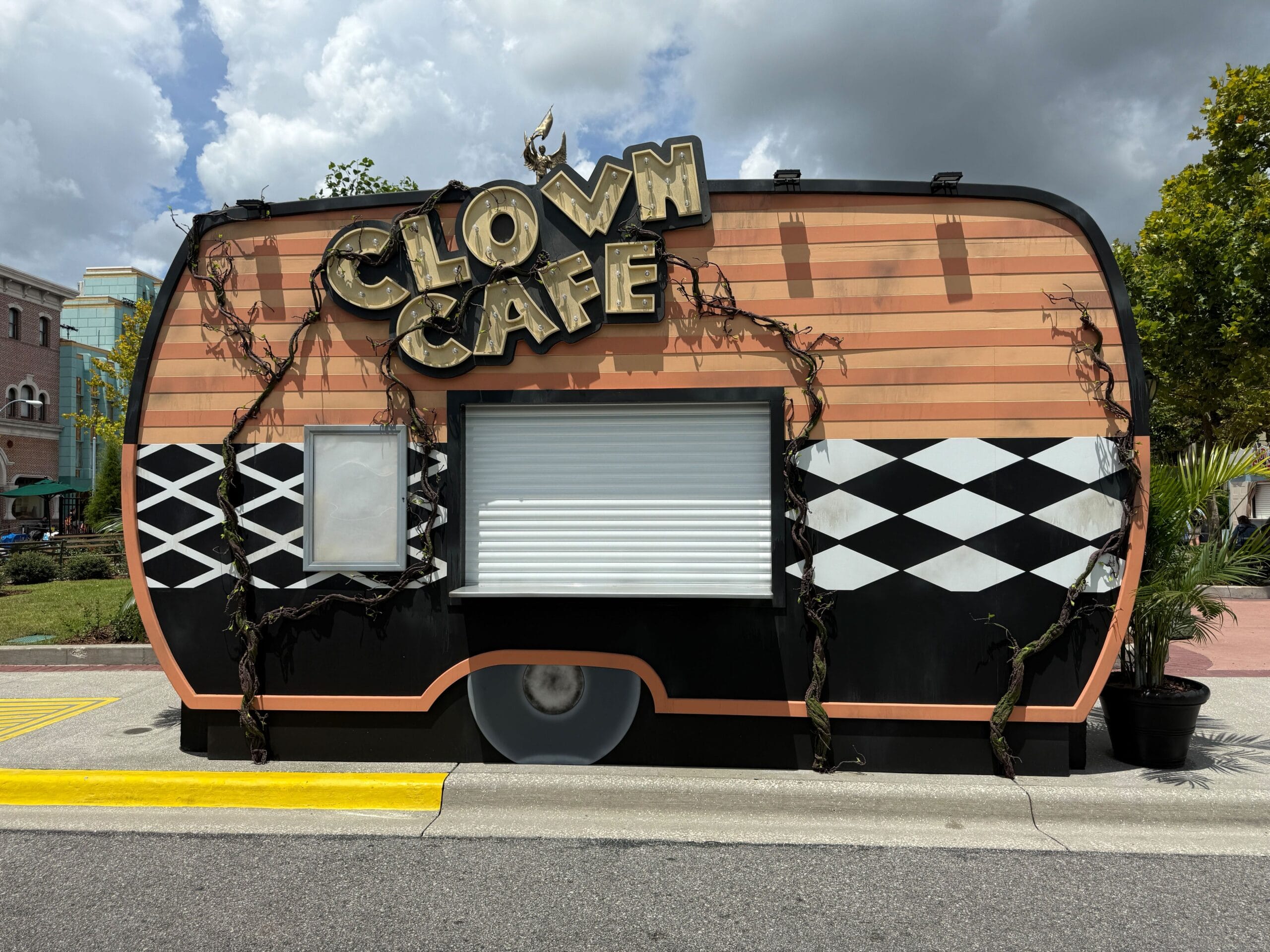 A closed Clown Café food trailer with a circus theme and vines, inspired by Terrifier's Clown Cafe, on a sunny day.