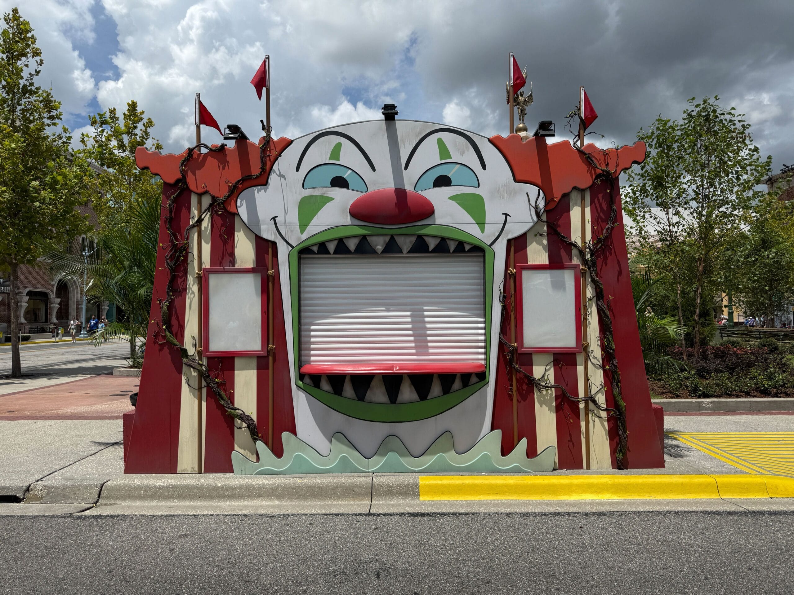 A closed carnival booth with a clown face, like Terrifier's Clown Cafe, its shuttered mouth under a cloudy sky.