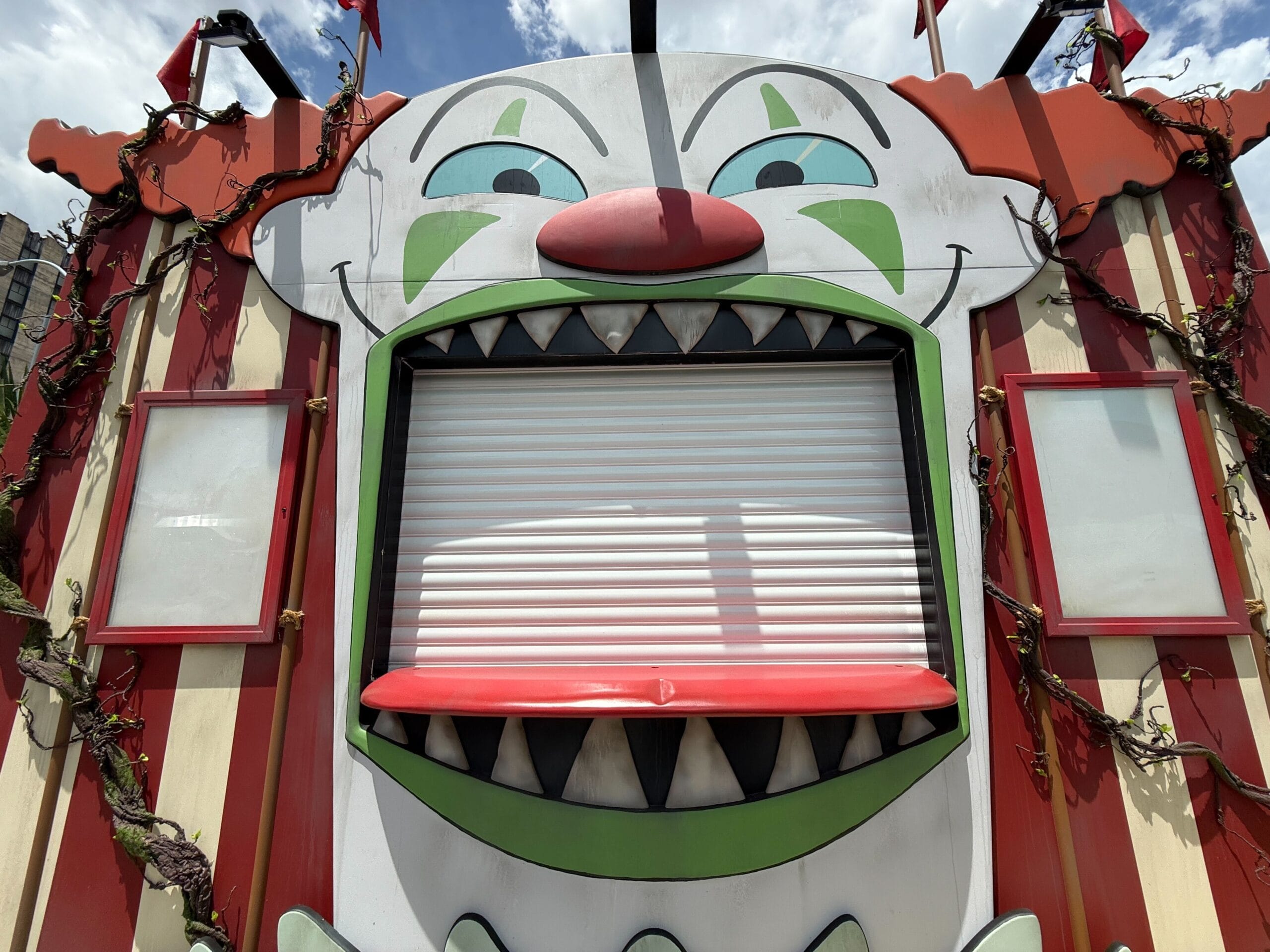 A Clown Cafe carnival booth with a closed shutter mouth sits under a partly cloudy sky.