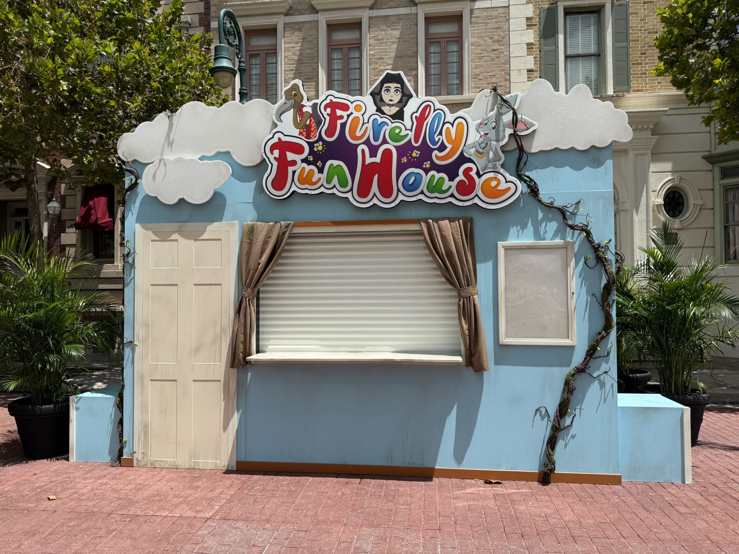 A closed Firefly Fun House booth with a Firefly Fun House Sign and vines, set along a city street at Halloween Horror Nights 34.