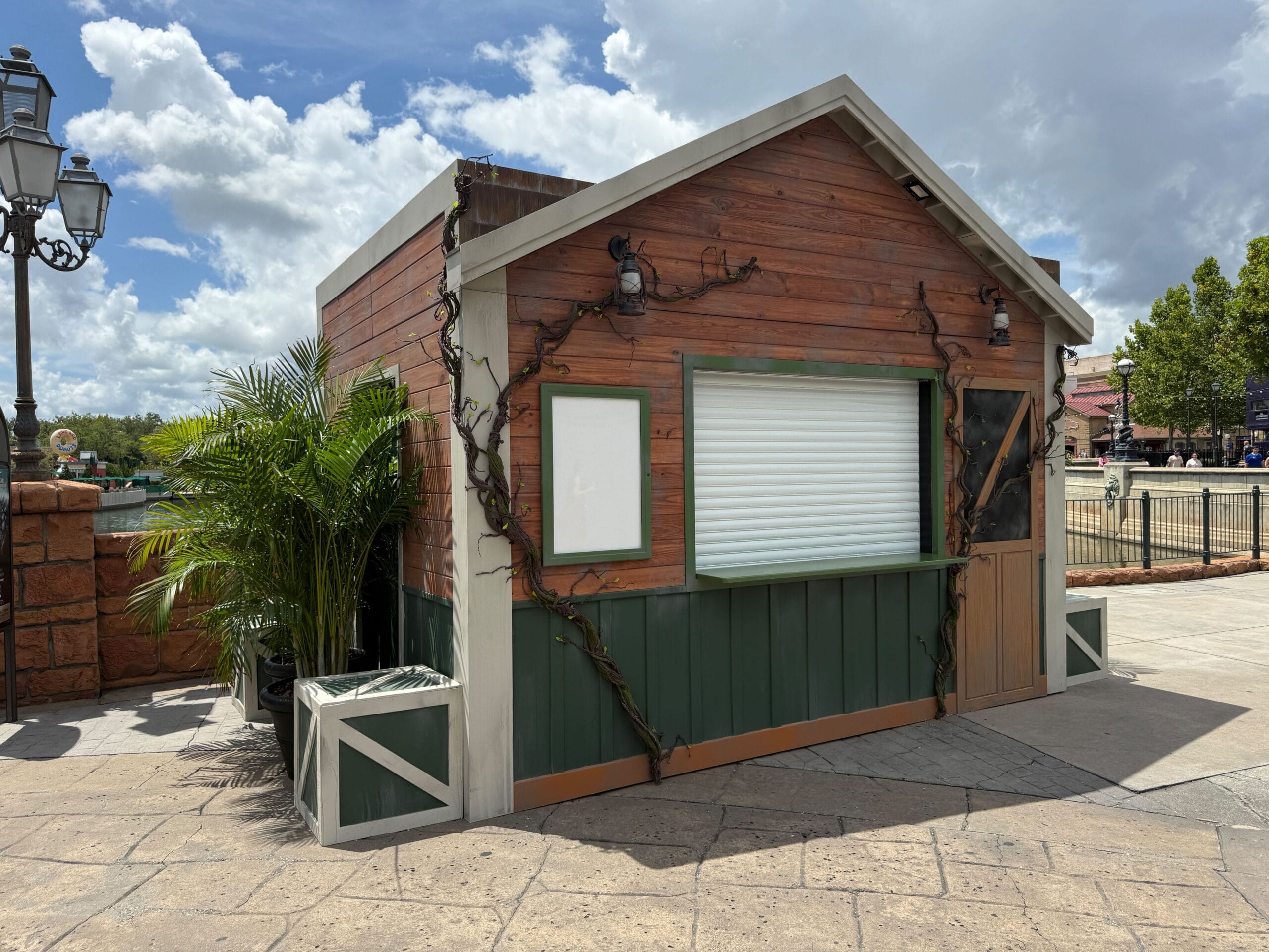 A closed wooden food kiosk with green trim, plants beside it, and a Terrifer's Clown Cafe sign in the background.