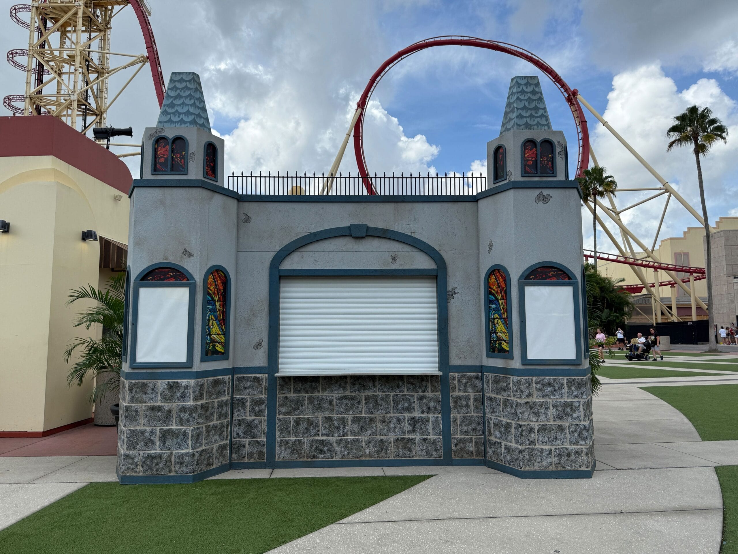 Gray castle-themed food booth with closed white shutter near a red coaster at Halloween Horror Nights 34.