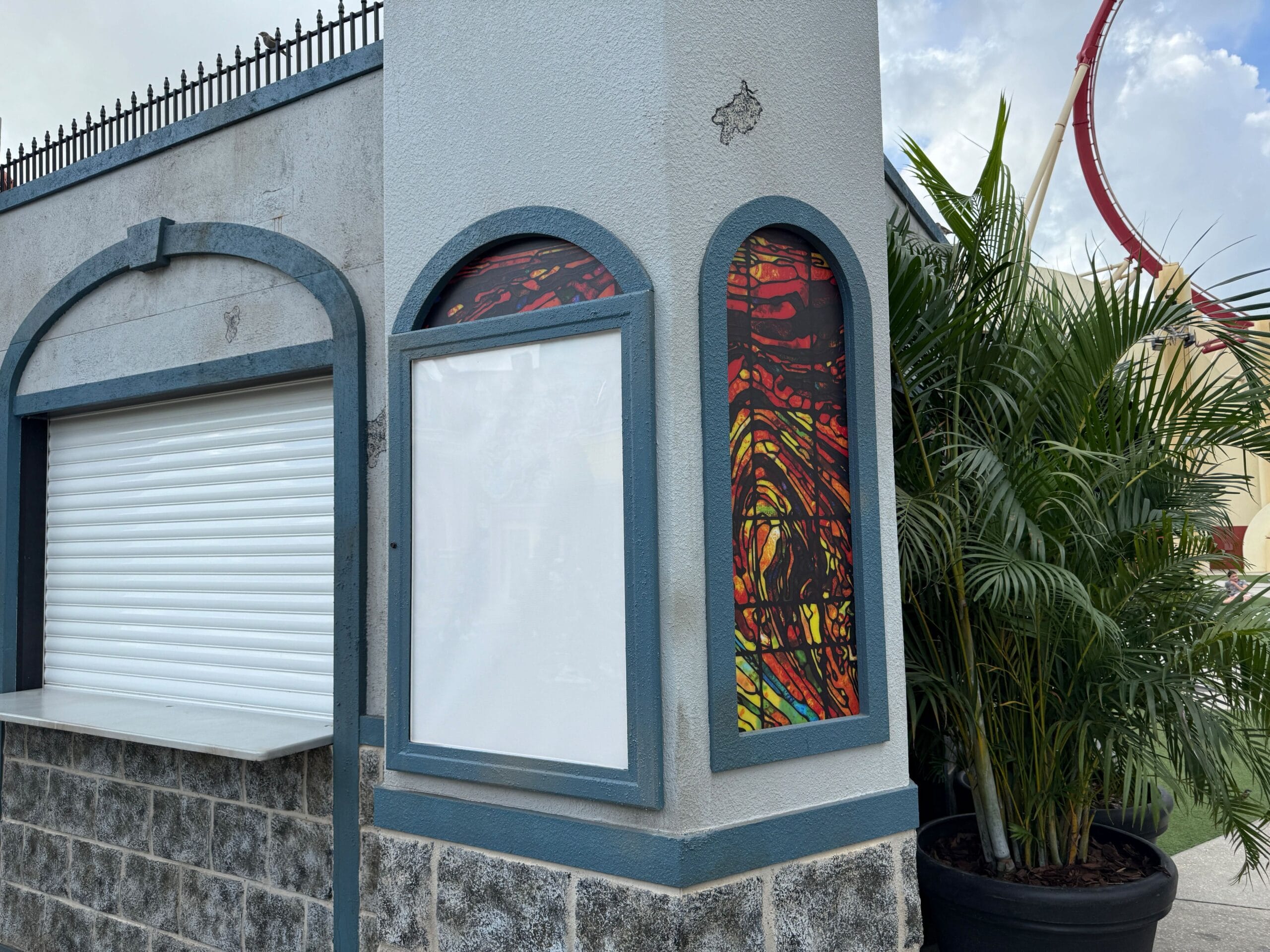 A blank sign is posted on a corner building near potted plants, evoking a Clown Cafe vibe from Halloween Horror Nights 34.
