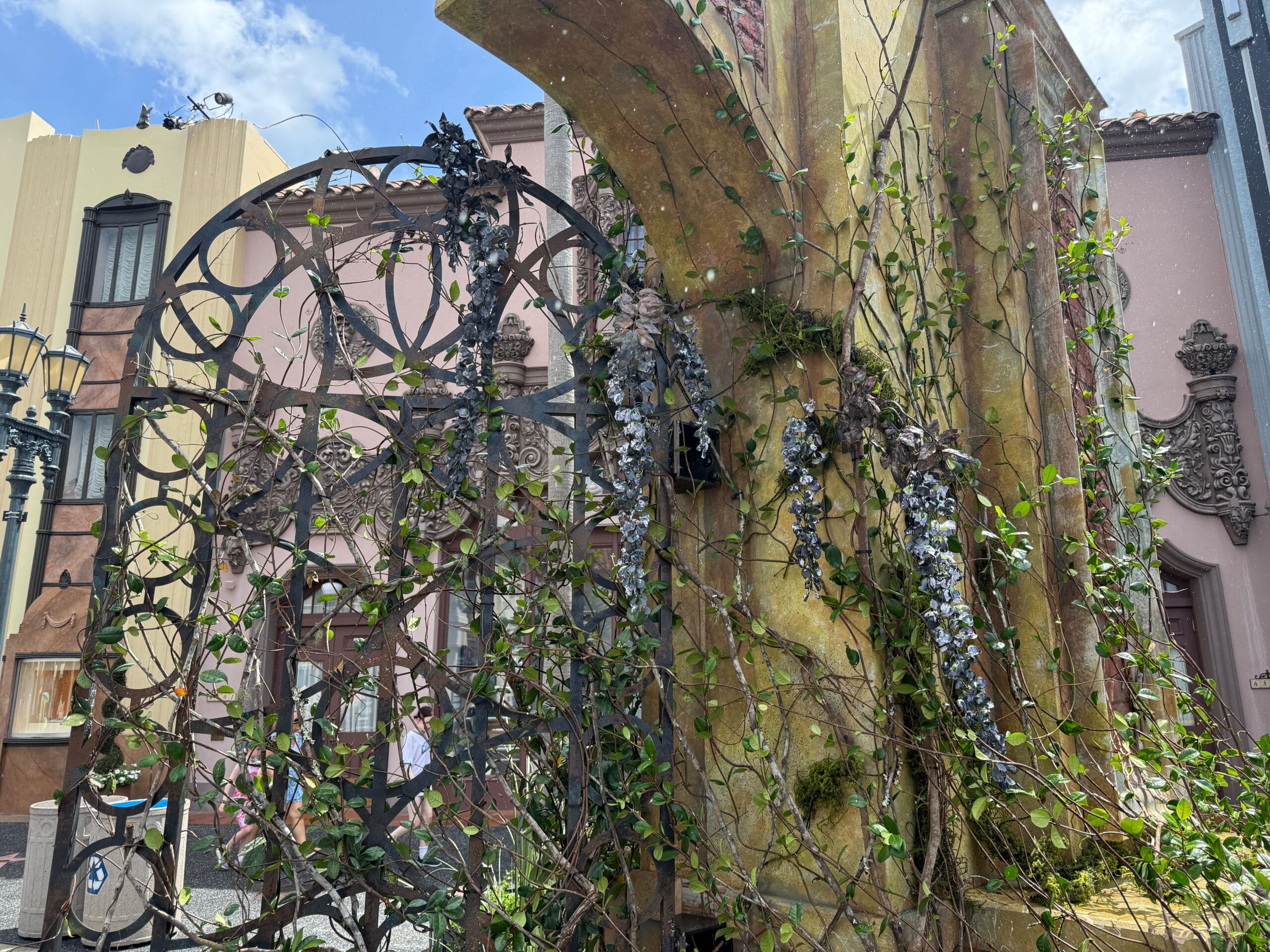 Rustic metal gate and stone wall with purple flowers, near a Clown Cafe sign for Halloween Horror Nights 34.