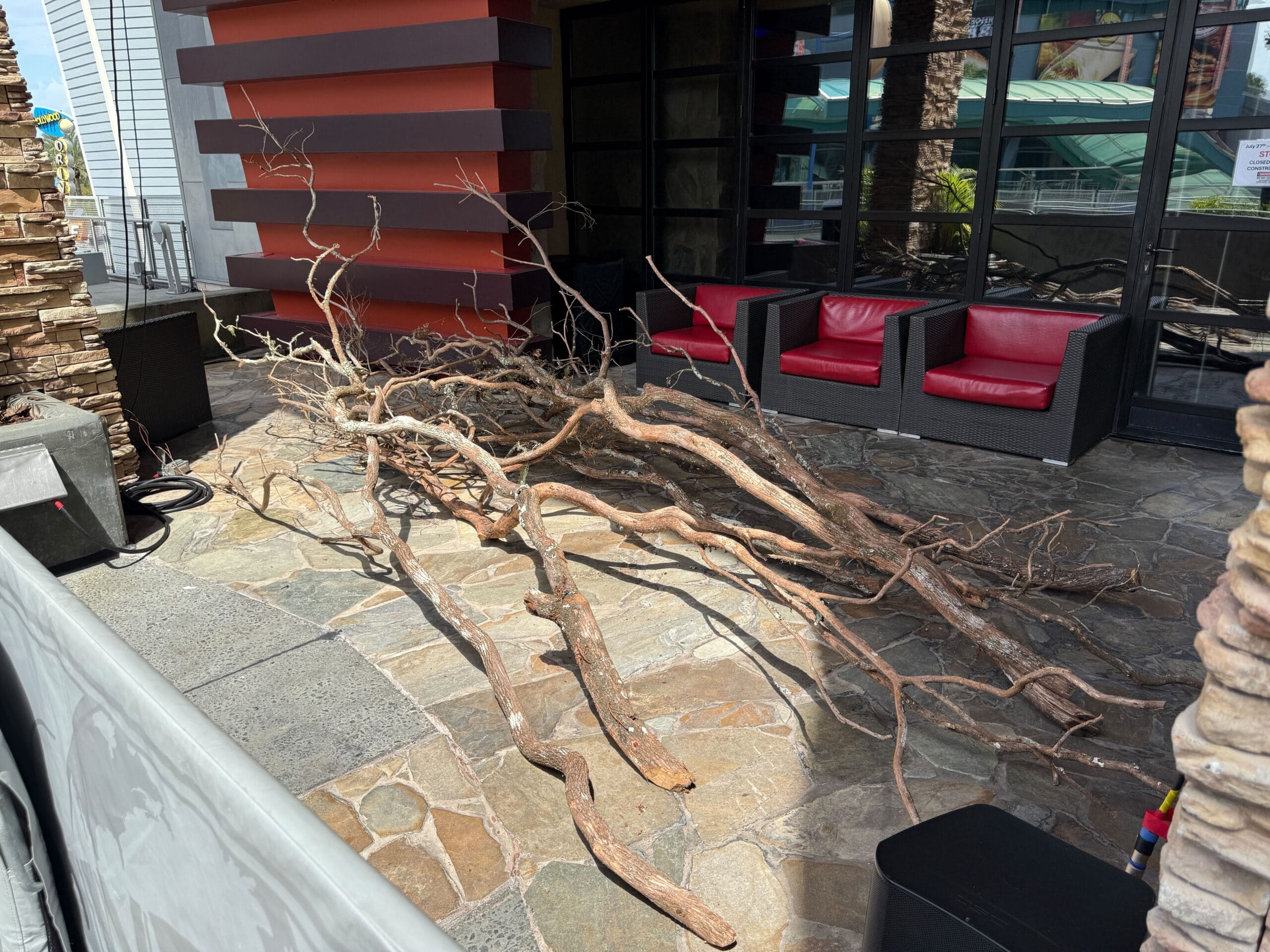 Large pile of dry tree branches on a stone patio near black chairs with red cushions at Halloween Horror Nights 34.