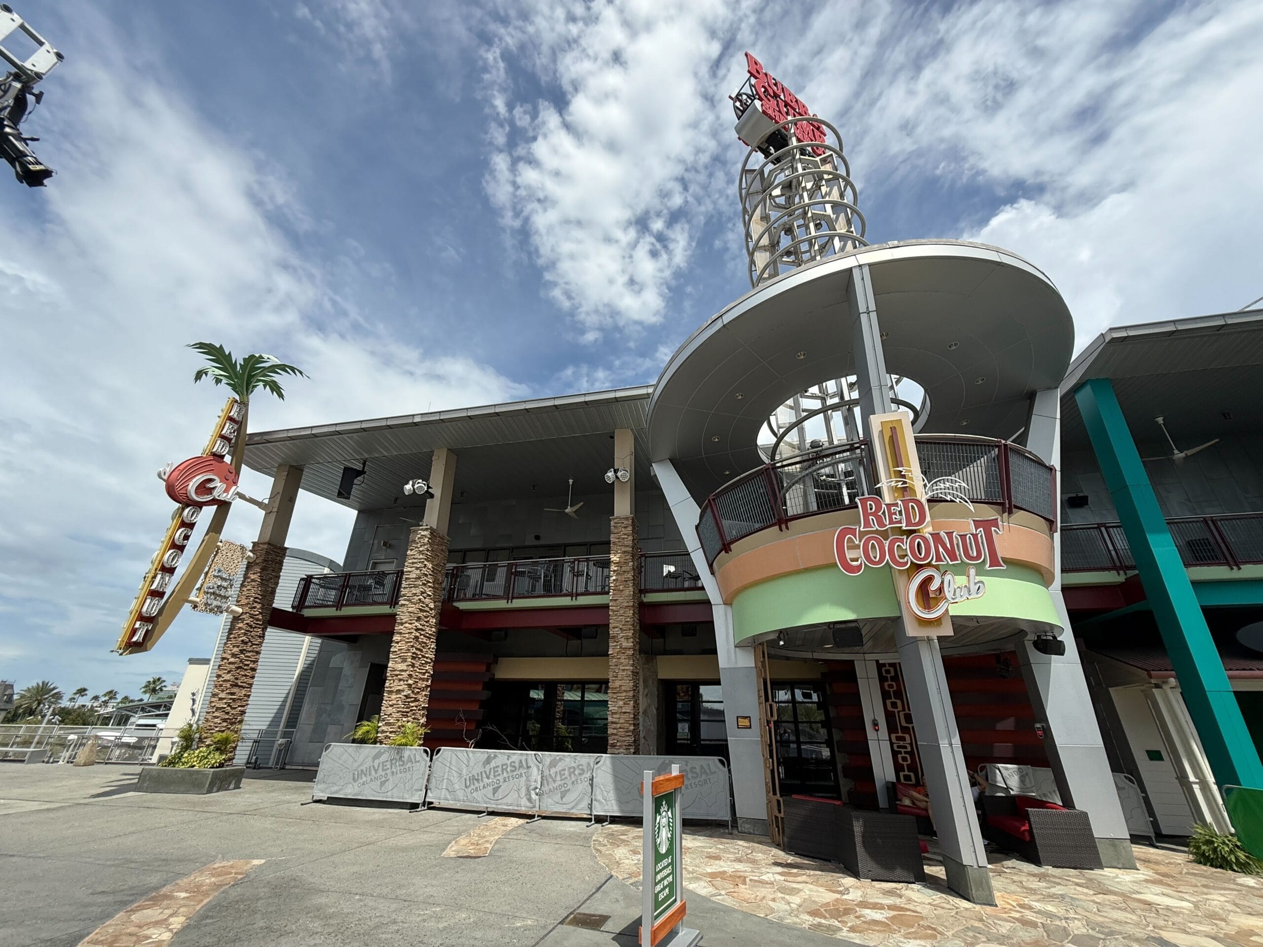 Red Coconut Club exterior with tall sign, palm tree, and a nod to Halloween Horror Nights 34 under a cloudy sky.