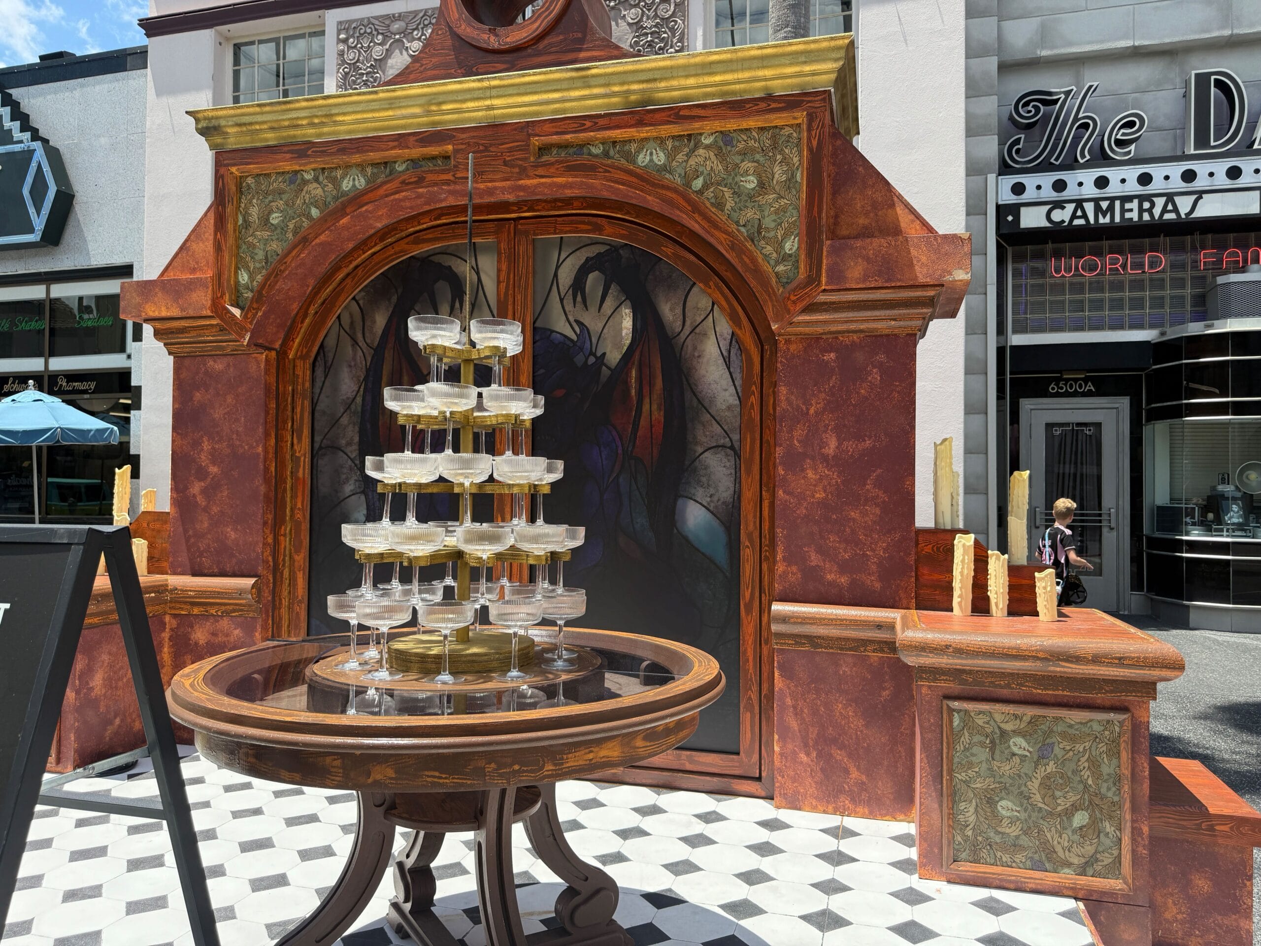 A tiered champagne glass tower stands on a round table in front of an ornate backdrop and building facade.