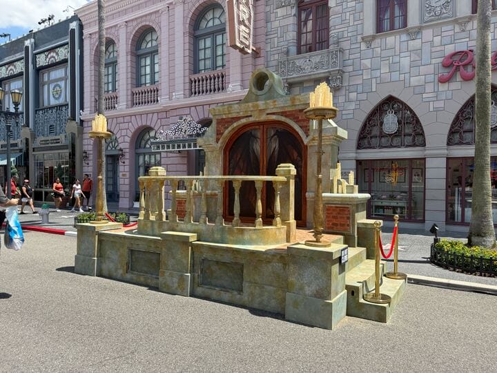 A decorative stone stage set with pillars and staircases stands on a street in front of ornate building facades.