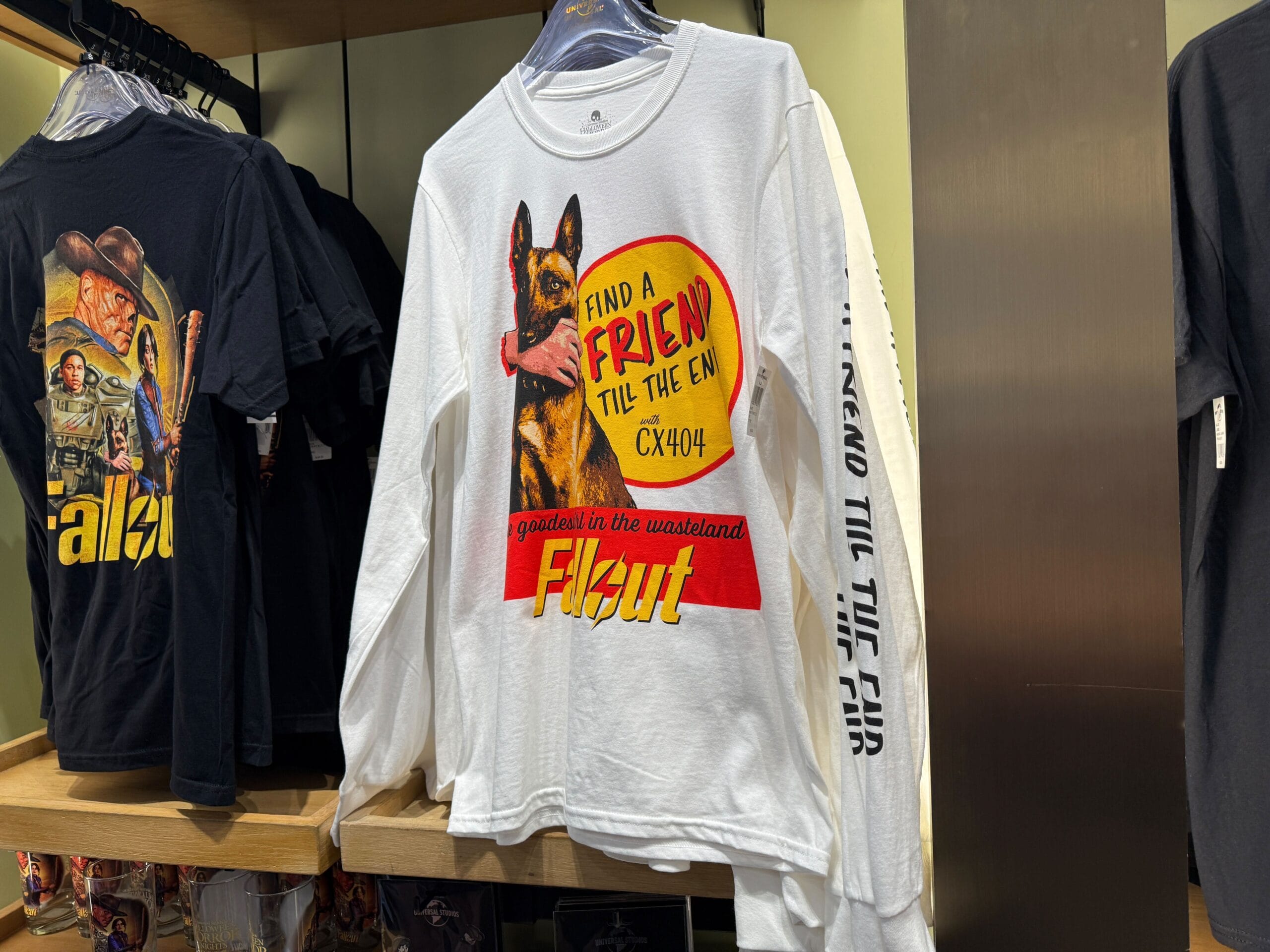 A white Fallout shirt with a dog graphic hangs in a Universal Orlando Resort store—perfect for HHN Merch 2025 fans.