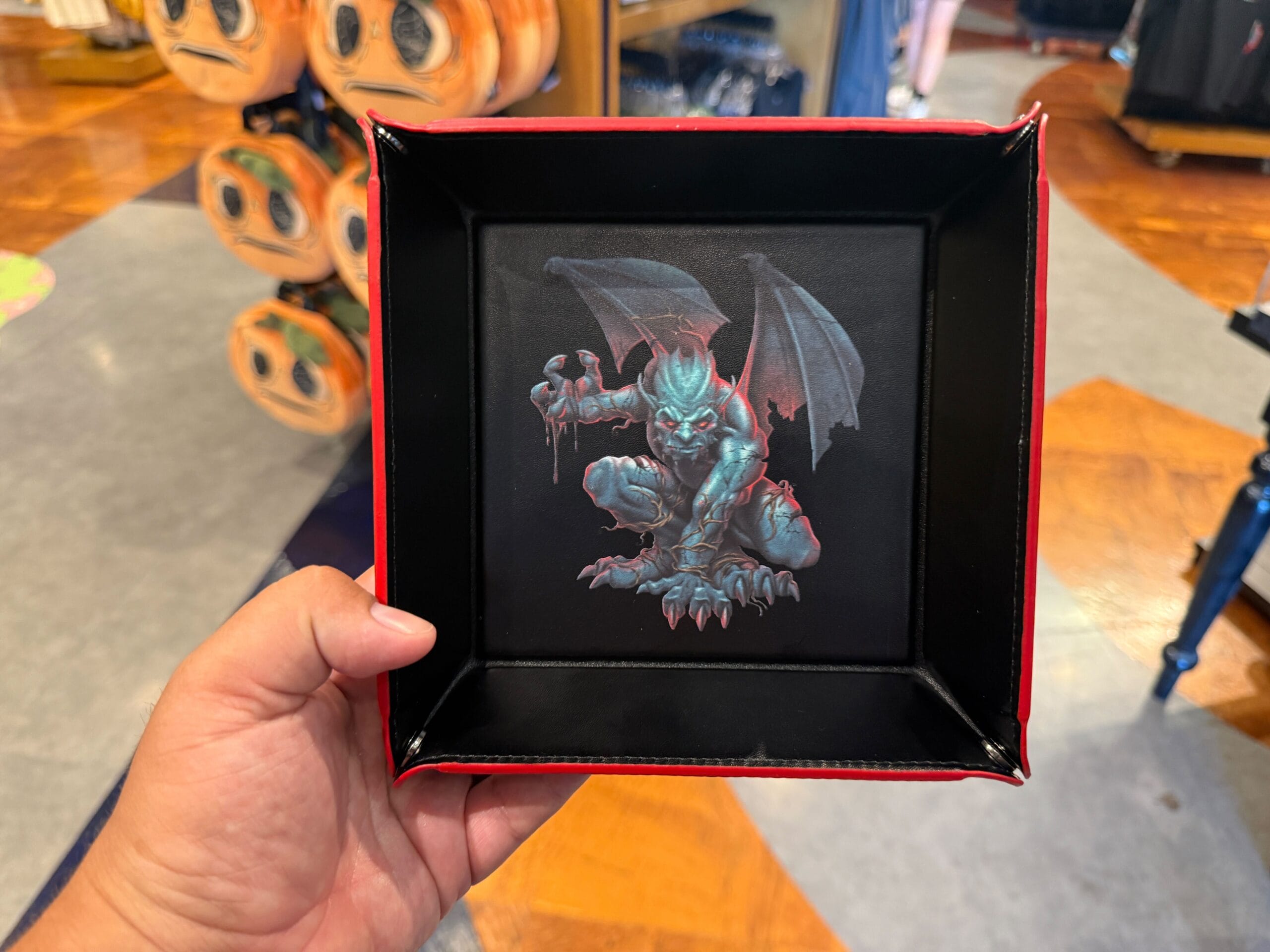 A hand holds a black tray featuring a menacing gargoyle design, part of the Halloween Horror Nights Merchandise.
