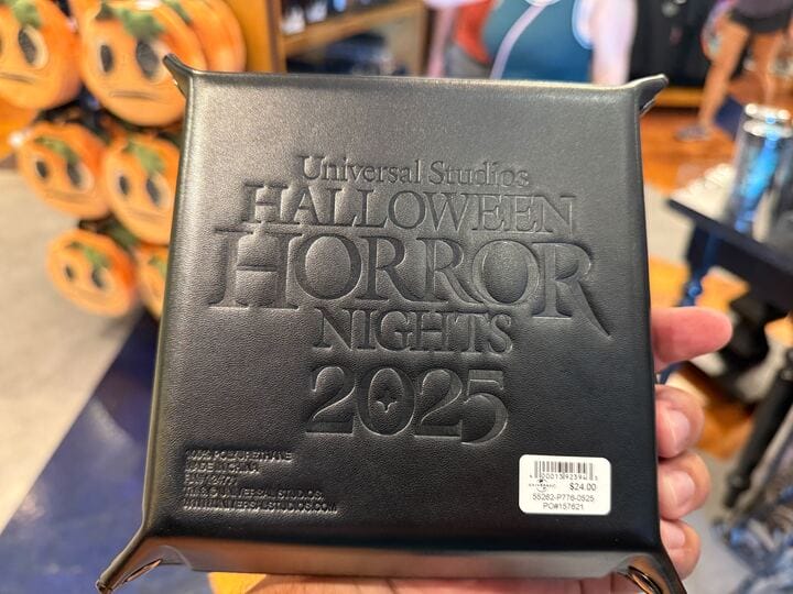A hand holds a black pouch embossed with "Halloween Horror Nights 2025," exclusive HHN Merch 2025 at Universal Orlando Resort.