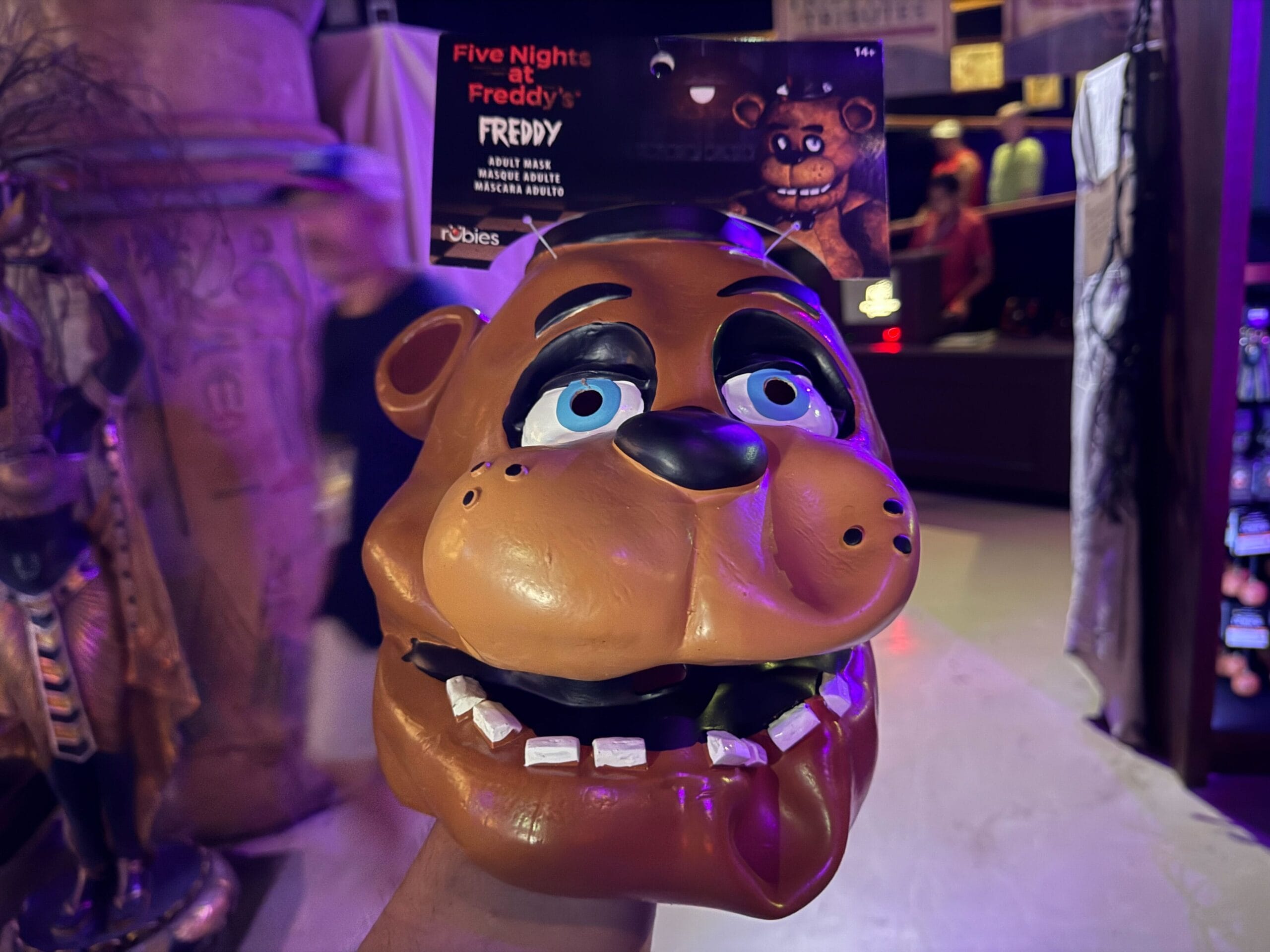A person holds a Freddy Fazbear mask from Five Nights at Freddy's in a dimly lit store.