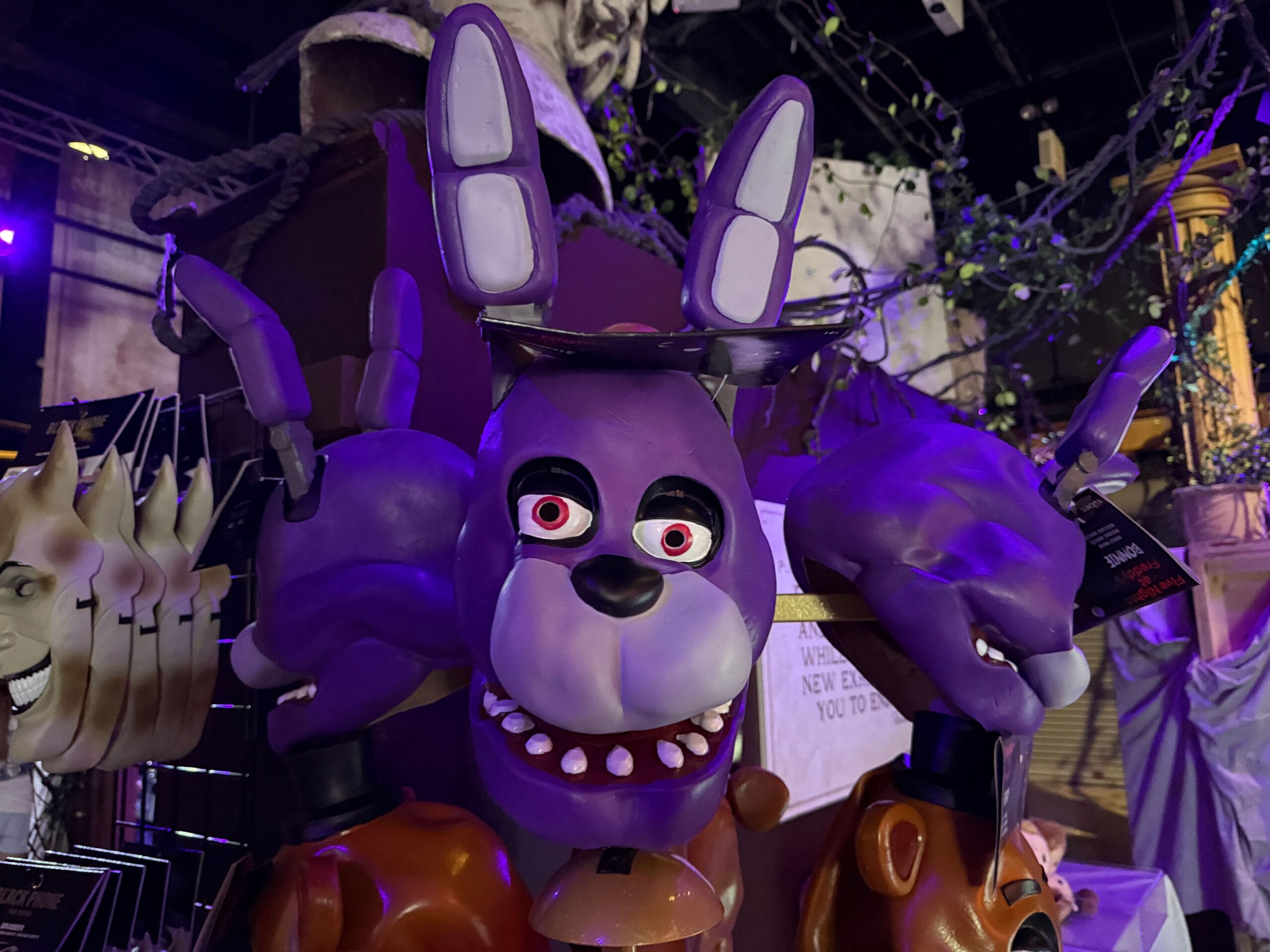 A purple animatronic bunny mask with exaggerated features is displayed among other masks in a dimly lit setting.