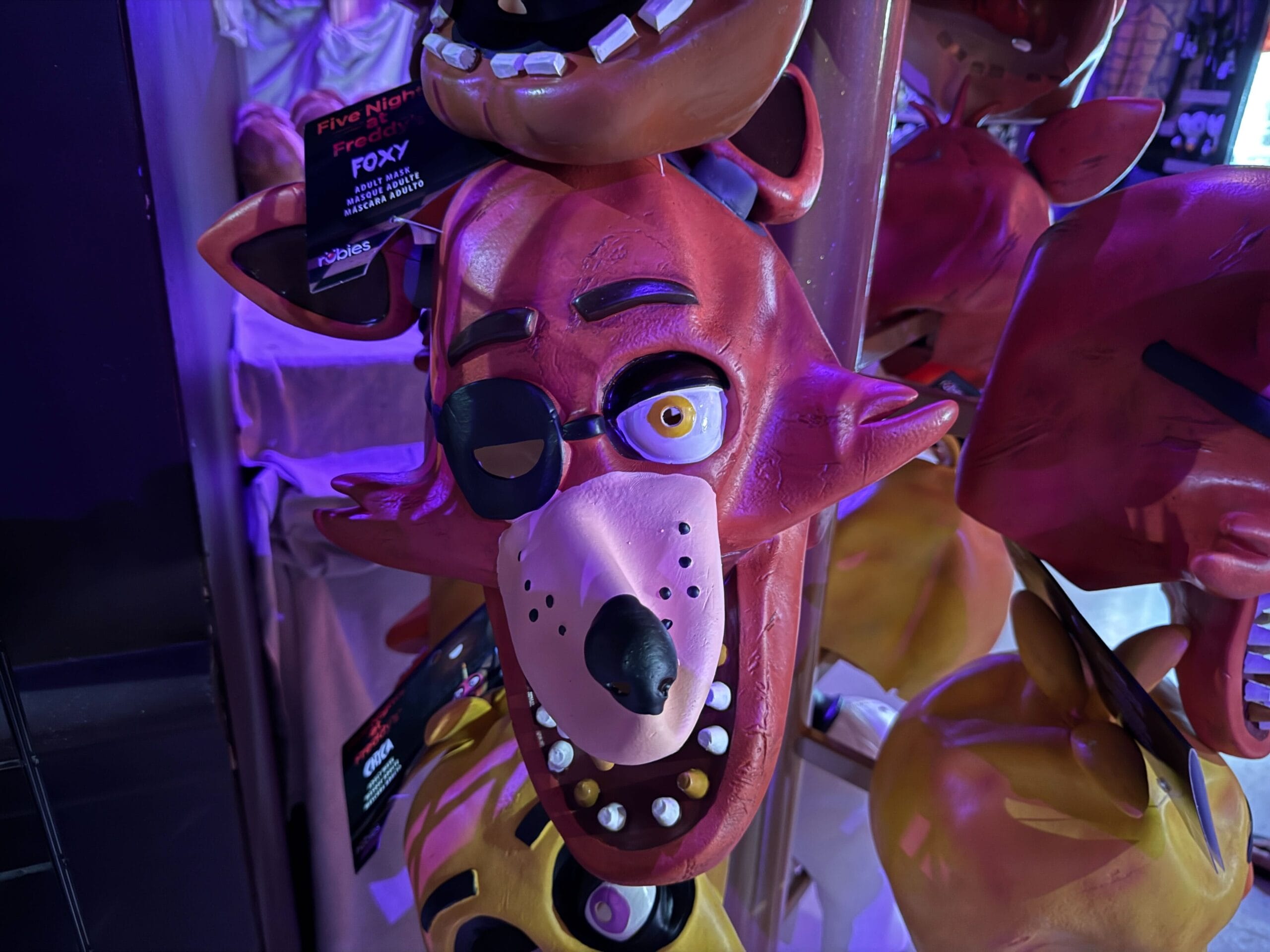 Close-up of a Foxy mask from Five Nights at Freddy’s, with an eye patch and big teeth, hanging for display.