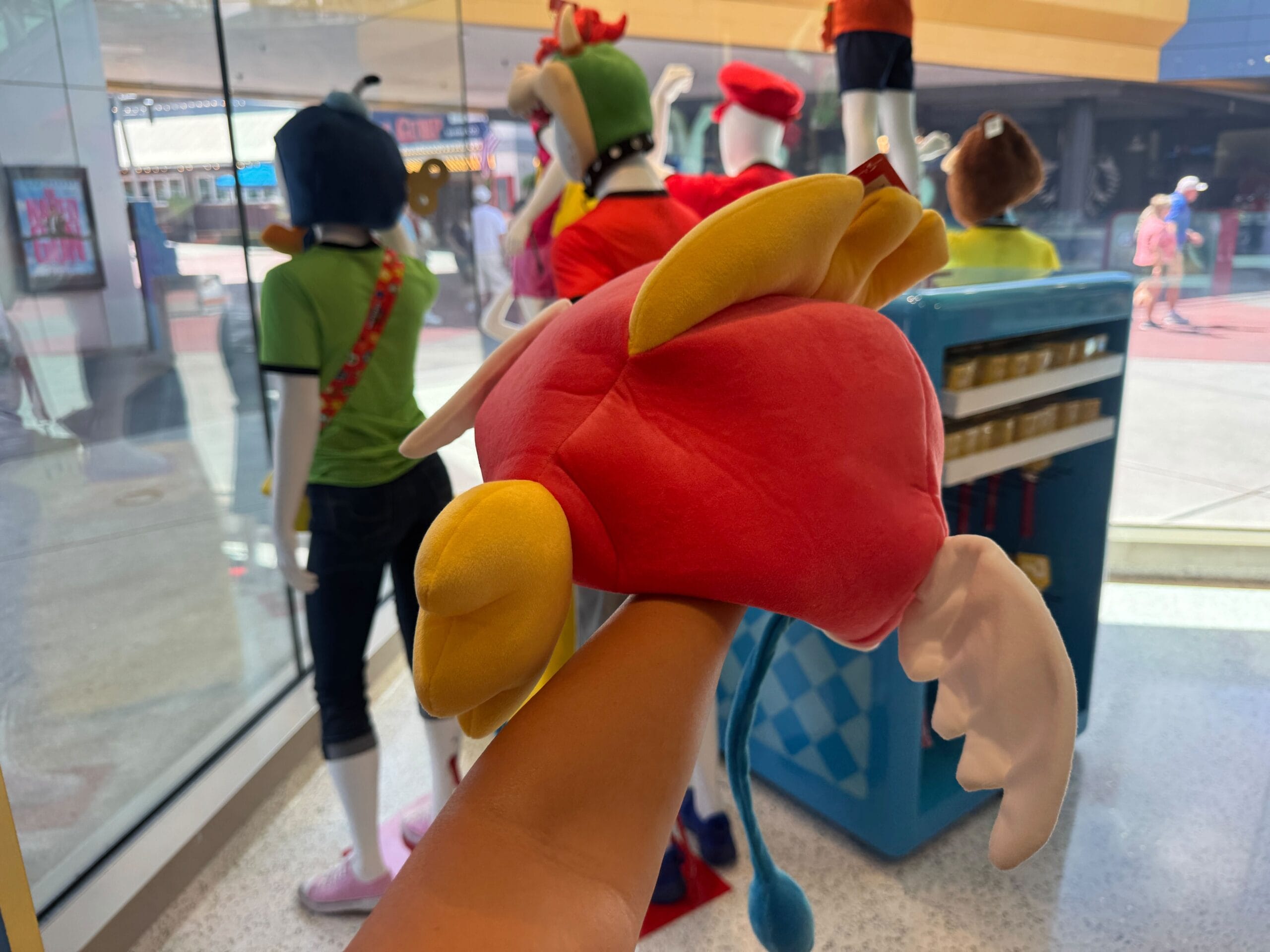 A hand holds a plush red bird with yellow wings; costumed mannequins pose in a Universal Studios window display.