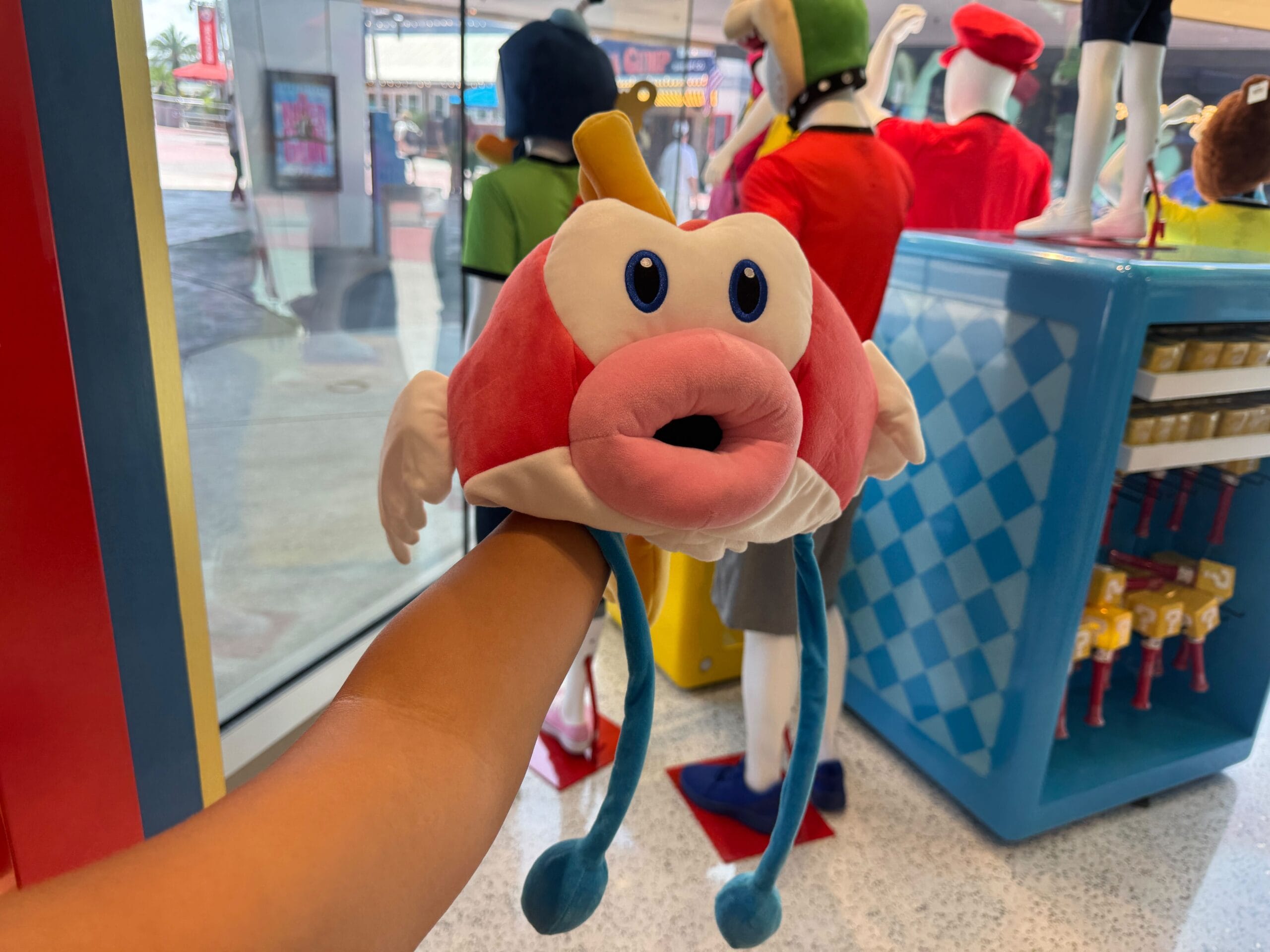 A person holds a Cheep Cheep Hat with big eyes and lips in a Universal Studios store with colorful displays.
